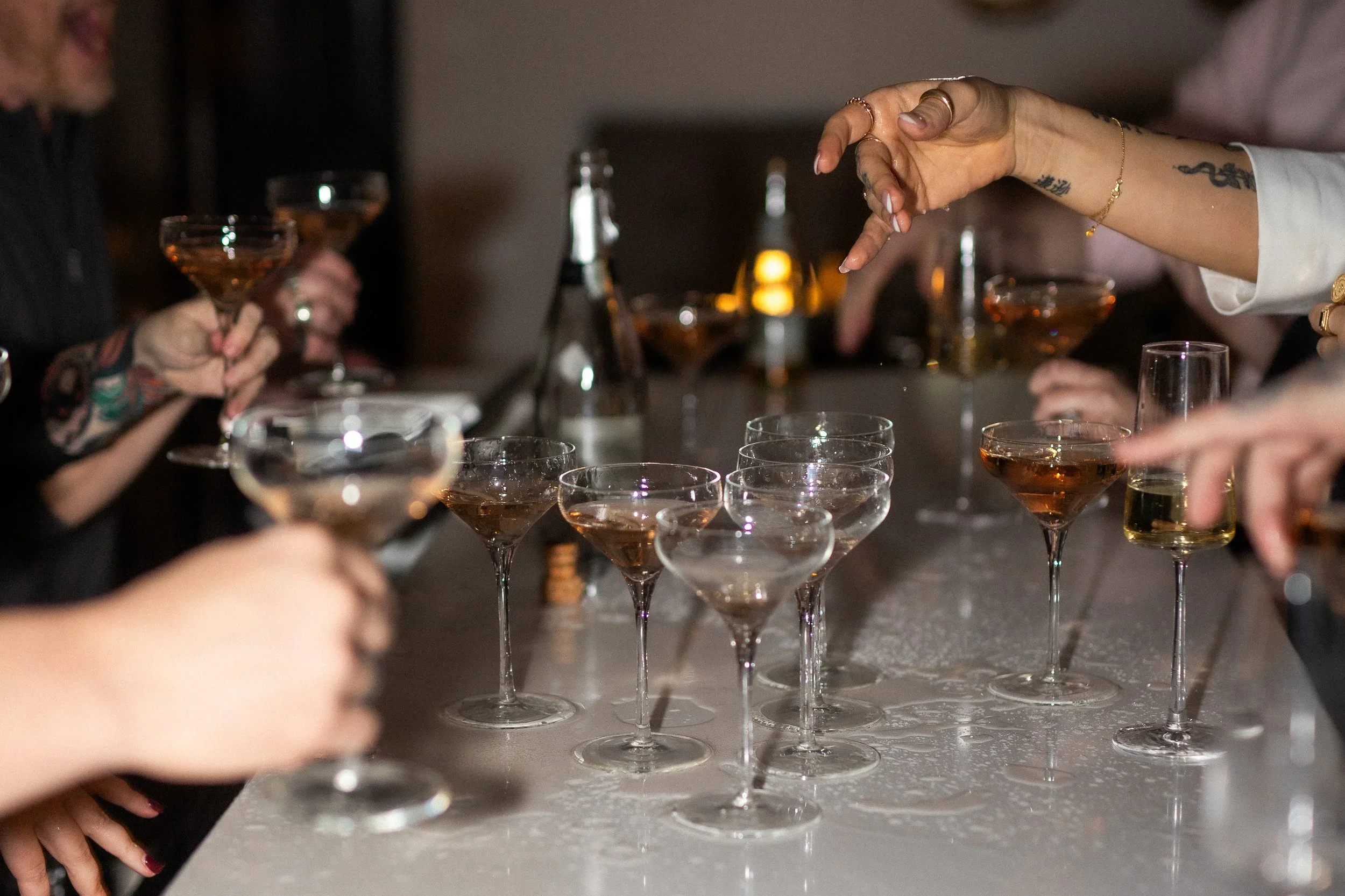 People holding glasses of champagne around a table with several empty glasses, bottles, and a decorative tablecloth.