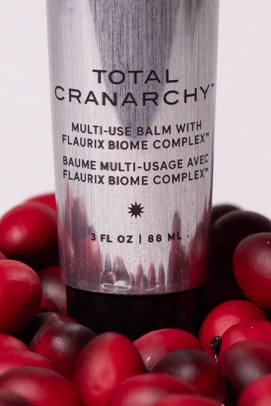 A metallic container of Total Cranarchy multi-use balm surrounded by small red grapes.
