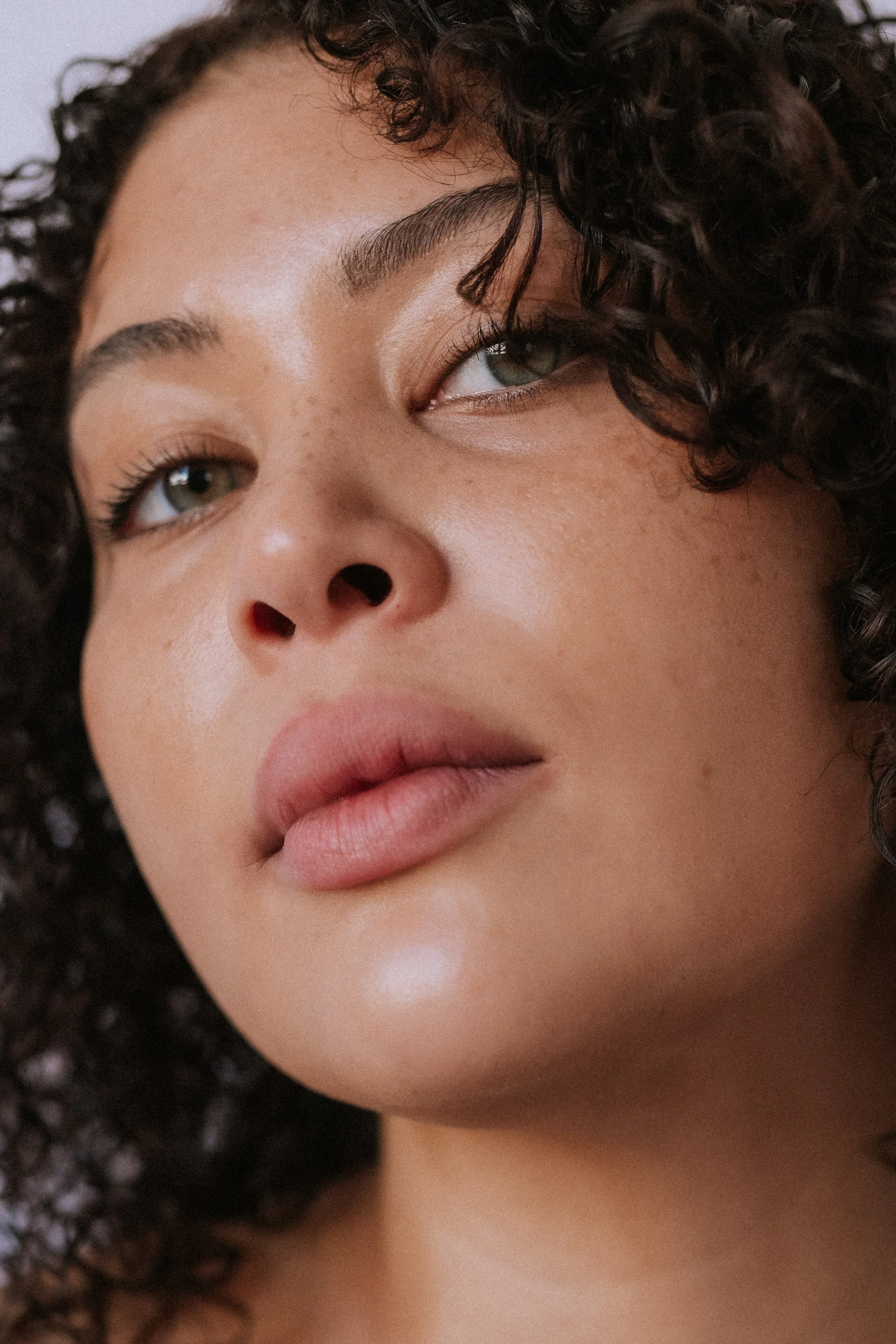 Close-up of a woman's face with curly hair, green eyes, and full lips.