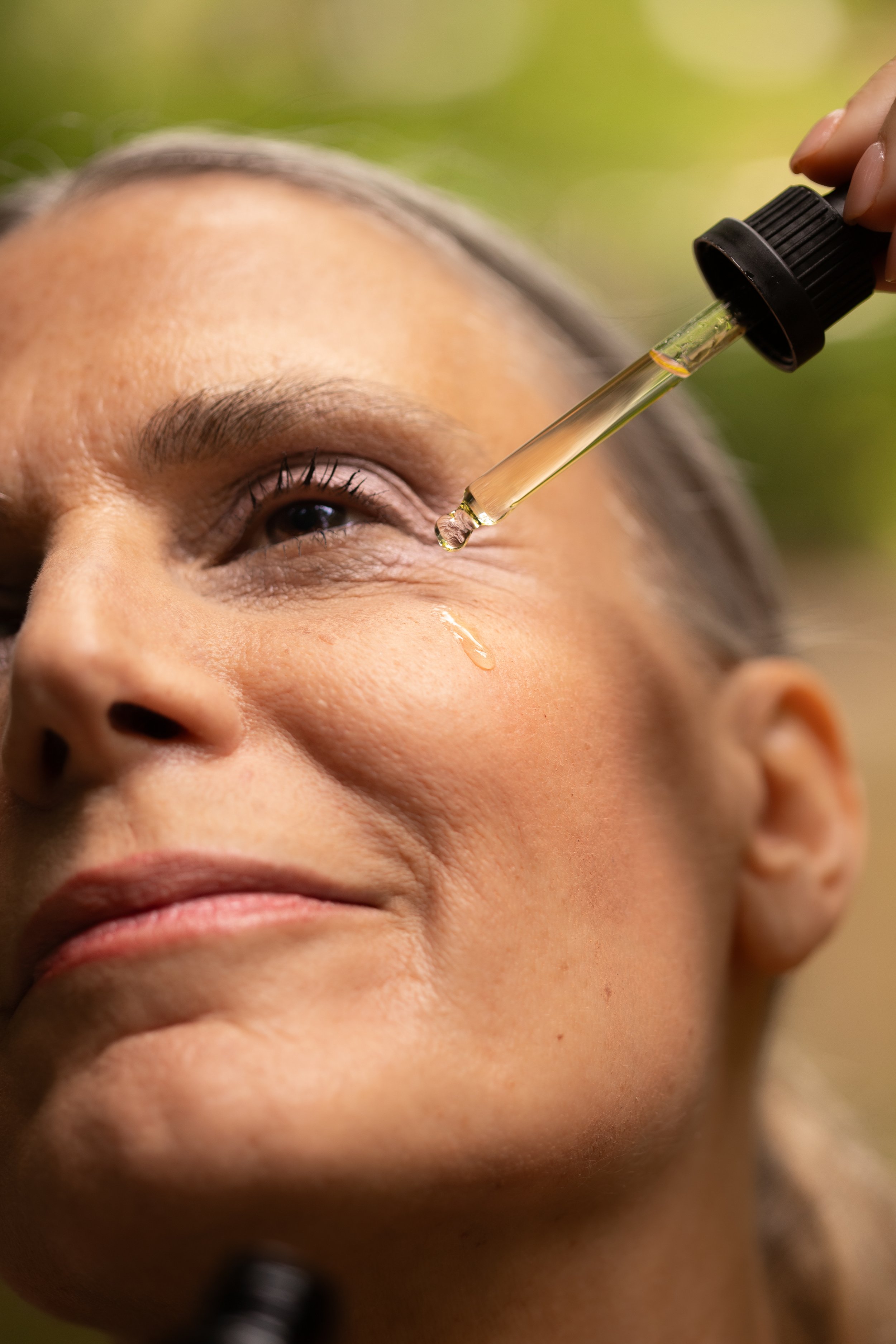 A woman receives a facial oil treatment with a dropper applying oil around her eye area.