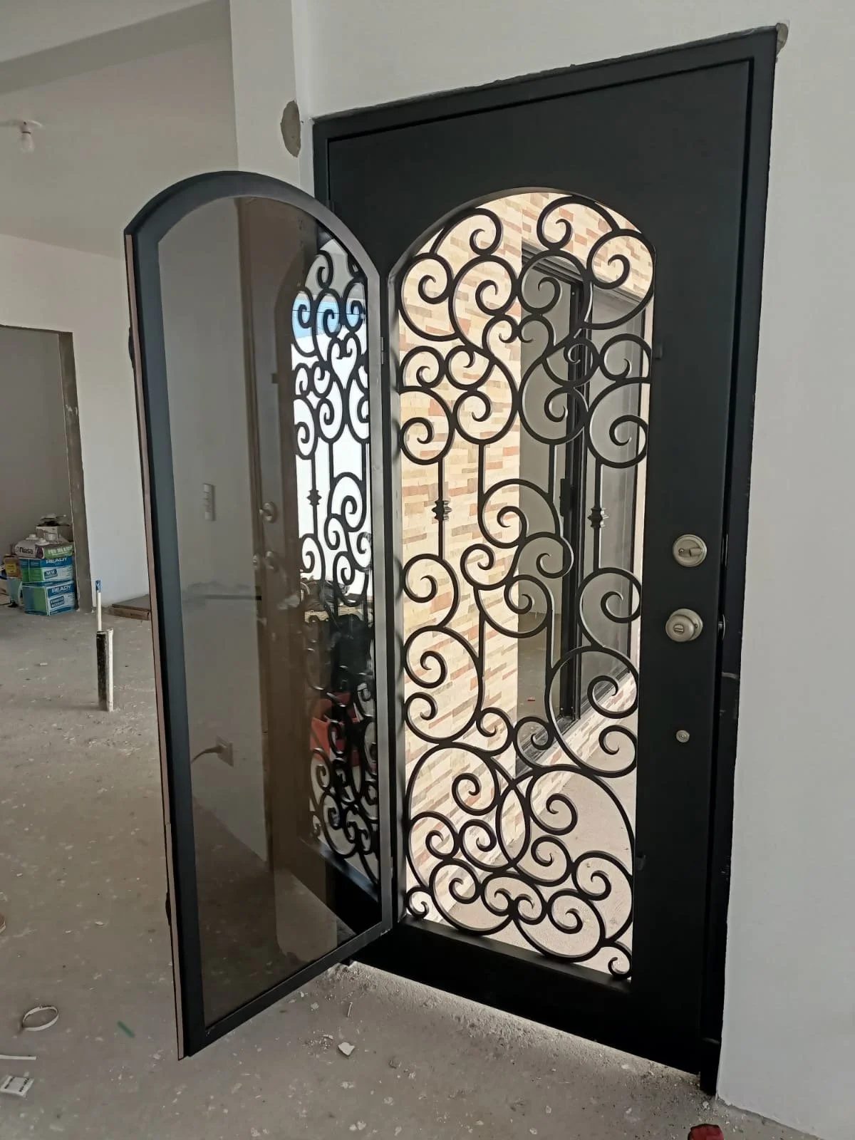 Black iron security door with decorative scrollwork, partially opened, showing the interior.