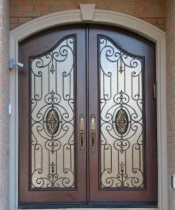 Front double metal gate with decorative ironwork and oval medallion designs, framed by a brick wall and archway.