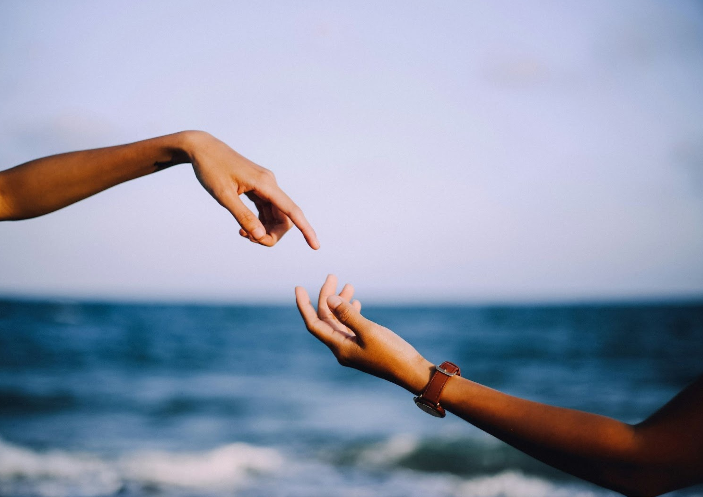 Two hands reaching toward each other against the backdrop of the ocean, symbolizing longing, connection, or emotional pursuit.