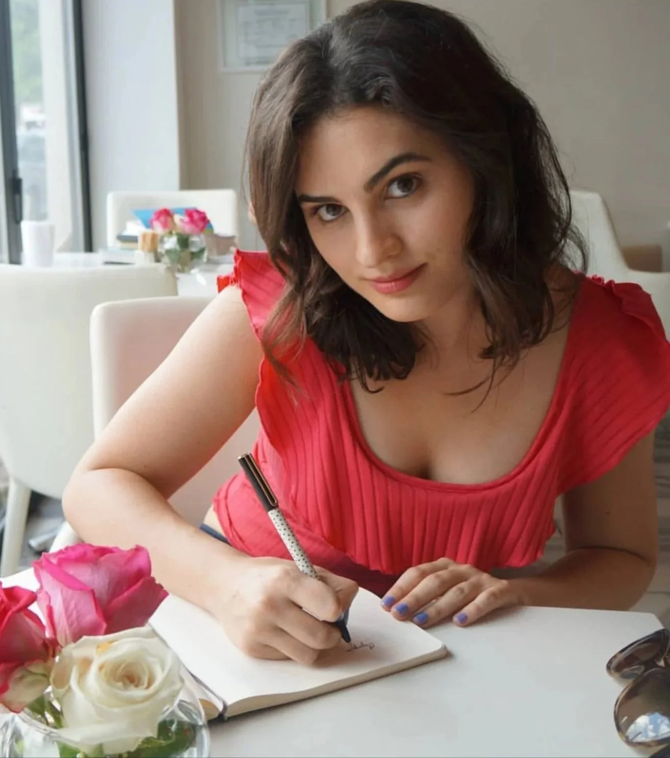 Olympia Georgeson sitting at a table, writing in a notebook with a pen.