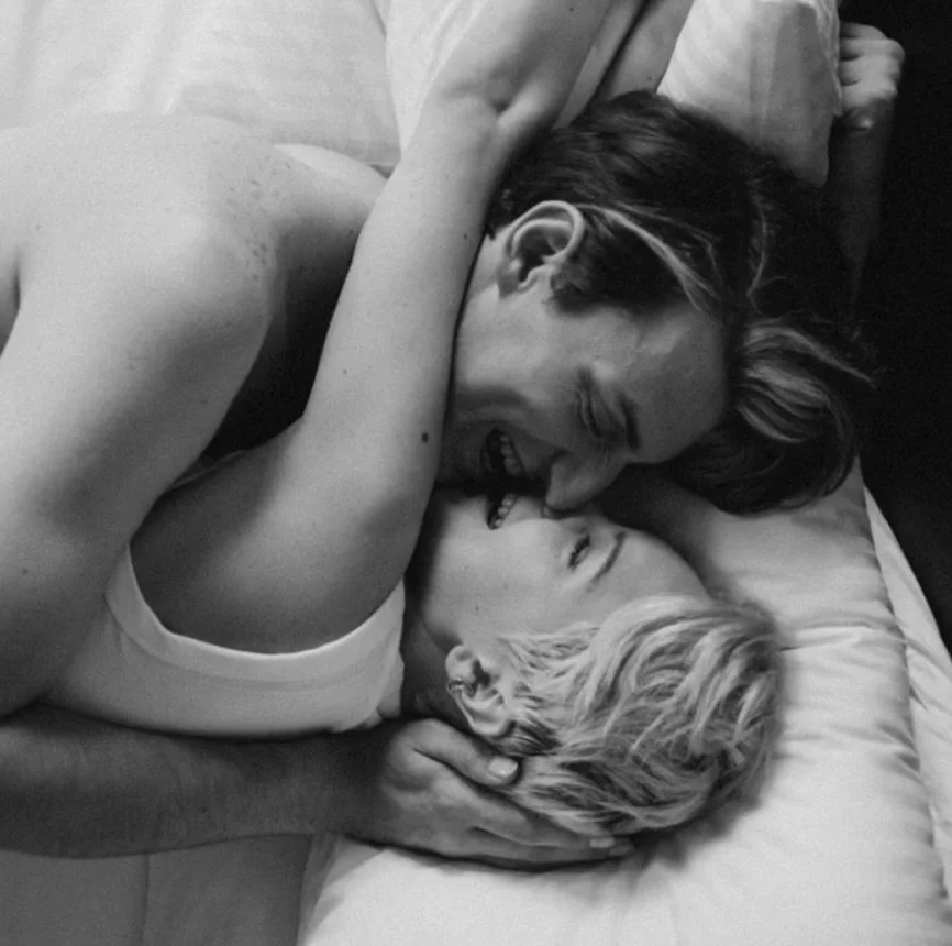 A couple smiling and embracing each other on a bed.