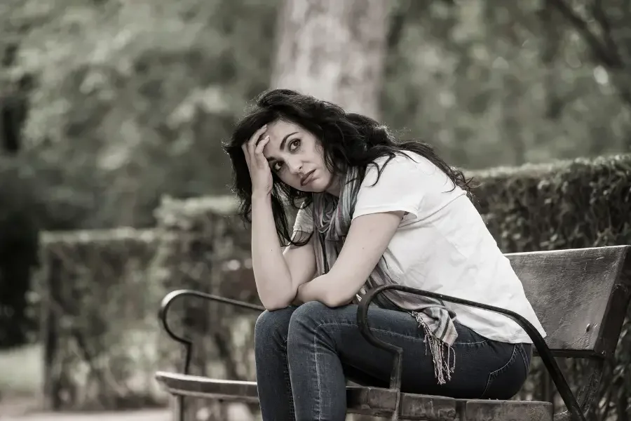 A woman sits on a bench, her head resting in her hands, conveying a sense of distress or contemplation.