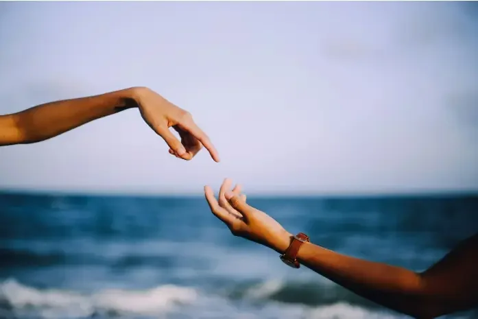 Two hands reaching out to each other against a beach backdrop, symbolizing connection and unity.