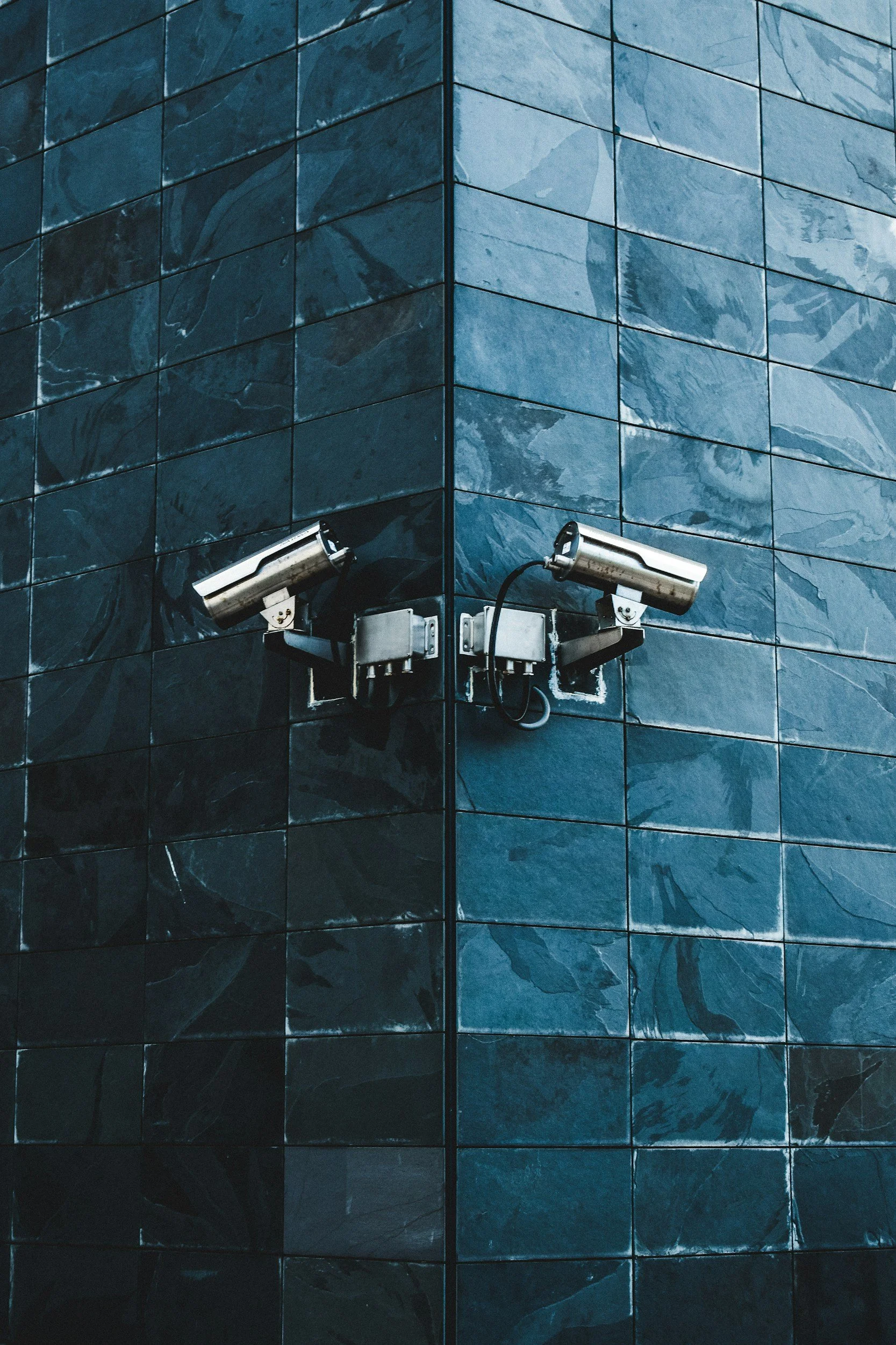 Two security cameras mounted on a blue tiled building corner.