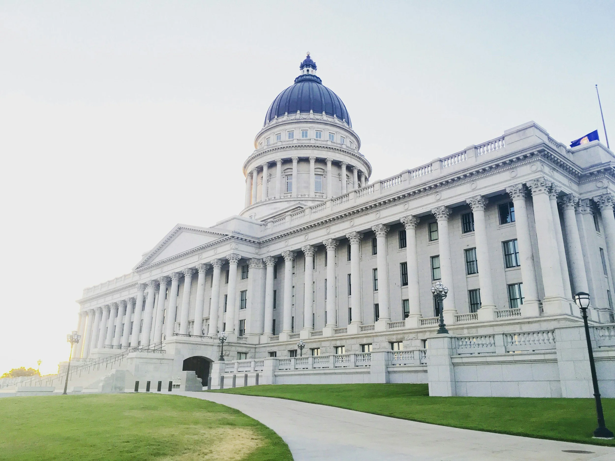The Arkansas State Capitol building with a domed roof, white exterior, and columns, surrounded by a green lawn and pathway