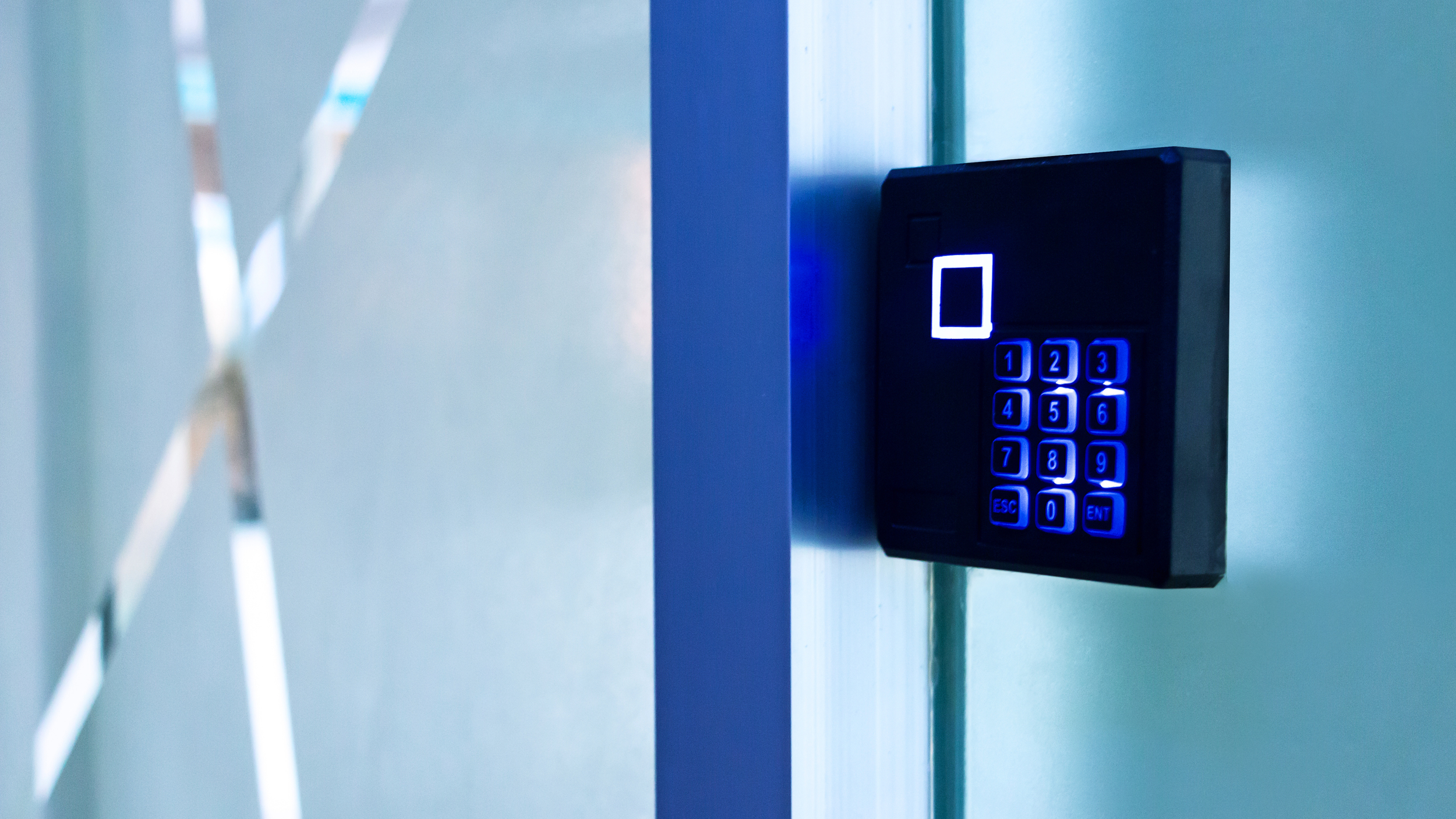 Access control keypad with illuminated blue buttons on a metal wall.