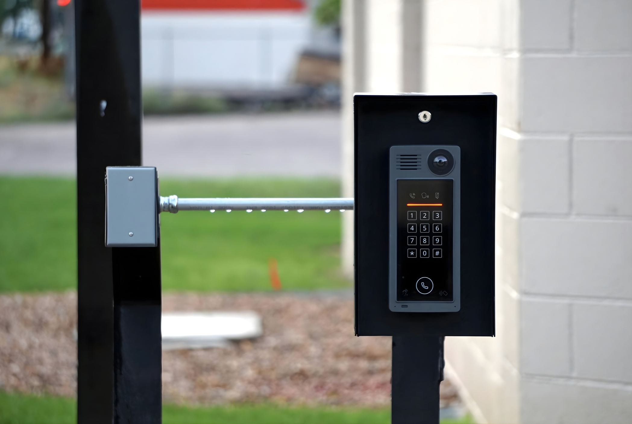 Front view of a modern intercom system with a keypad and a camera mounted on a black post outside a building.