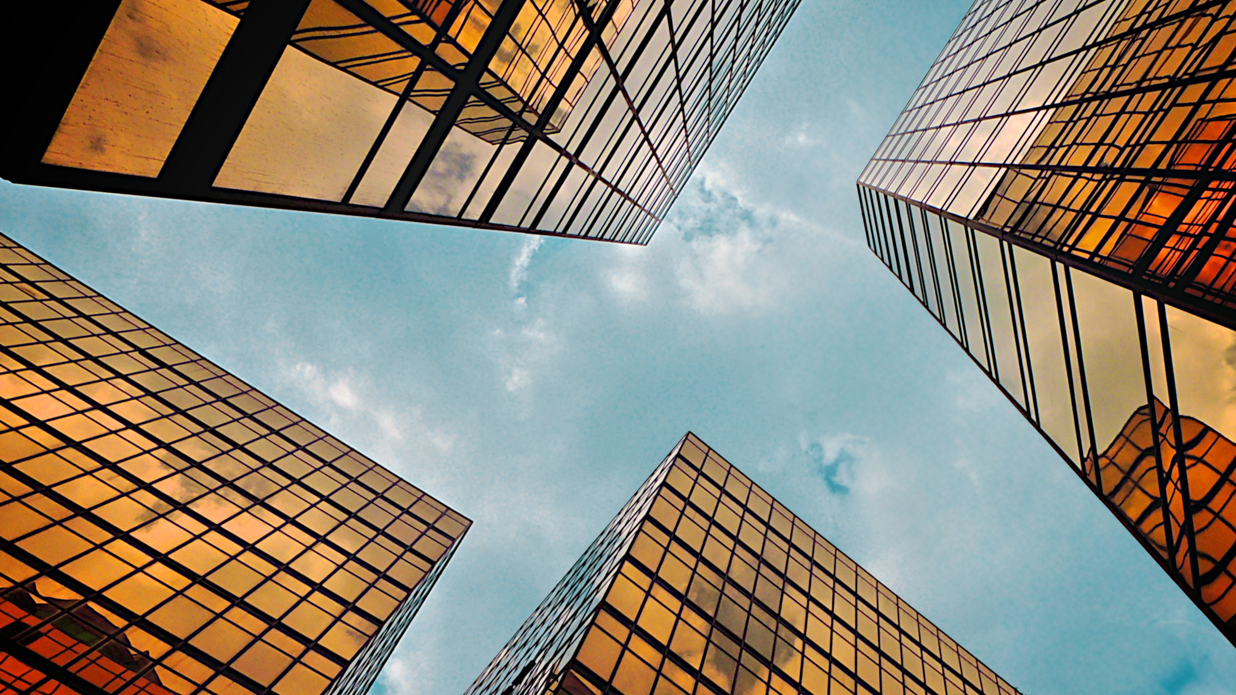 Looking up at tall glass office buildings with reflective windows, showing the sky and clouds.