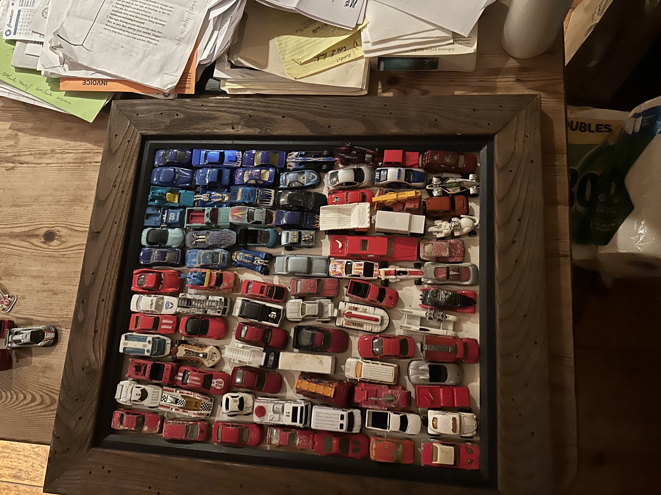 Collection of miniature toy cars arranged in a display case on a wooden table.