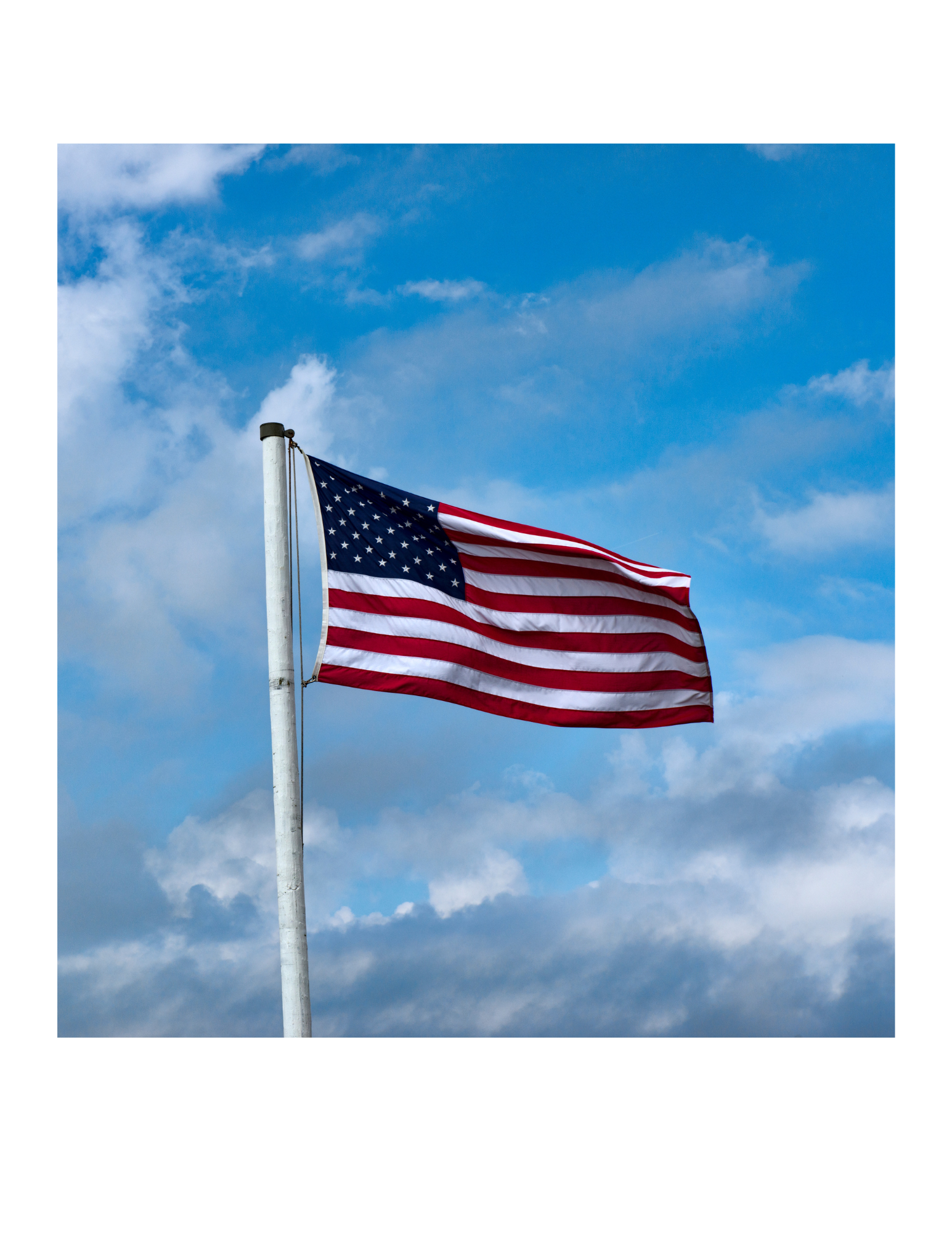 American flag waving in the wind against a blue sky with clouds.