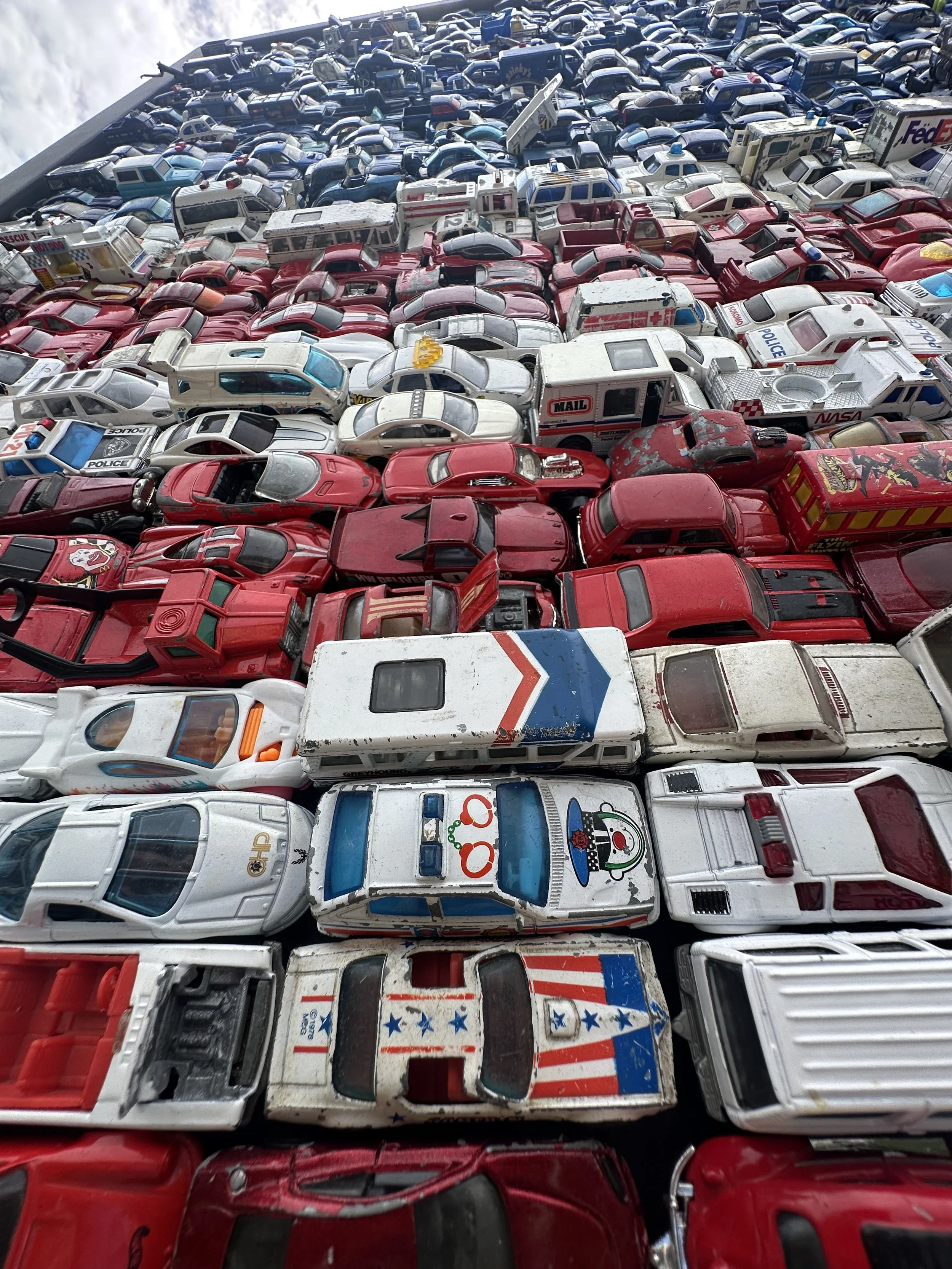 A large collection of toy cars, arranged in rows by color, with red, white, and blue vehicles prominently visible.