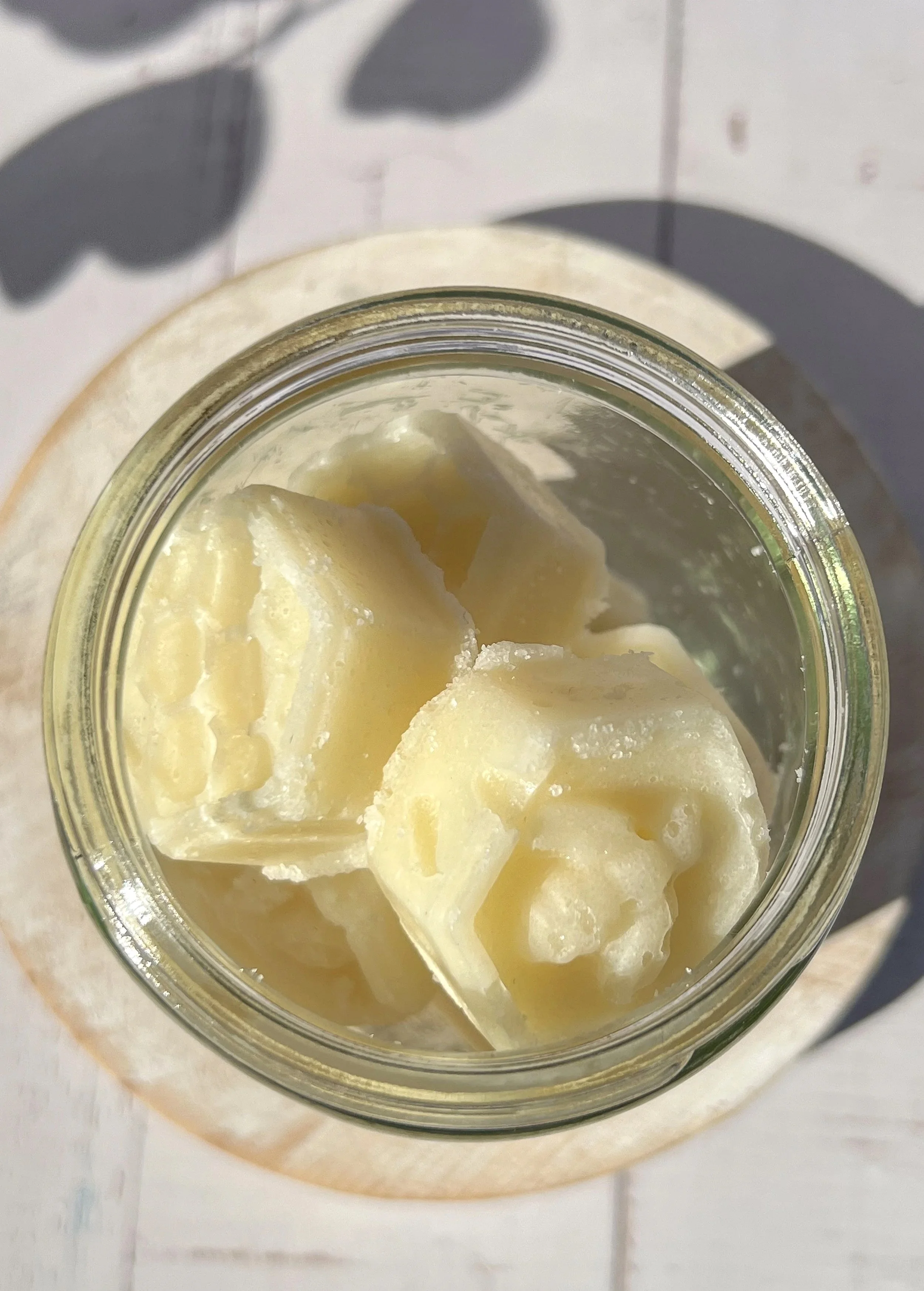 Close-up of a jar filled with chunks of white chocolate on a wood surface, with a shadow of leaves on the background.