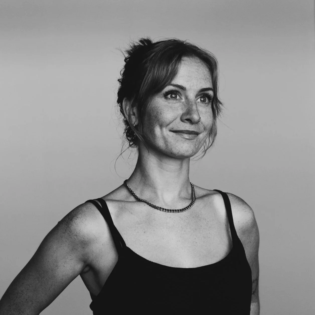 Black and white portrait of a smiling woman with short hair, wearing a black tank top and a necklace, against a plain background.