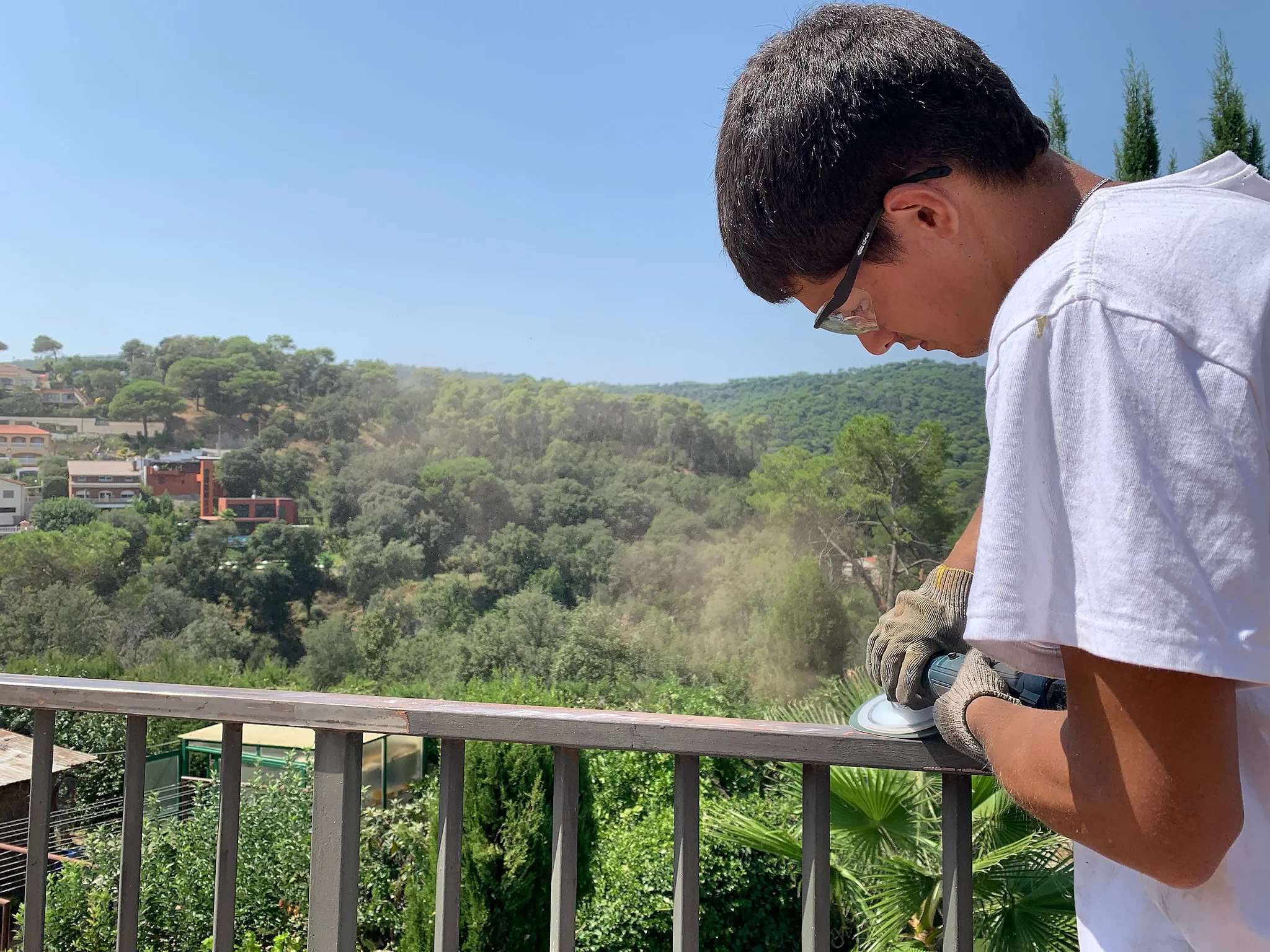 Trabajador moliendo la capa superficial de una baranda de metal y así prepararla para restaurar pintando.