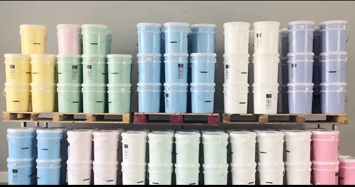 Multiple stacks of pastel-colored buckets arranged on wooden pallets in a warehouse or storage room.
