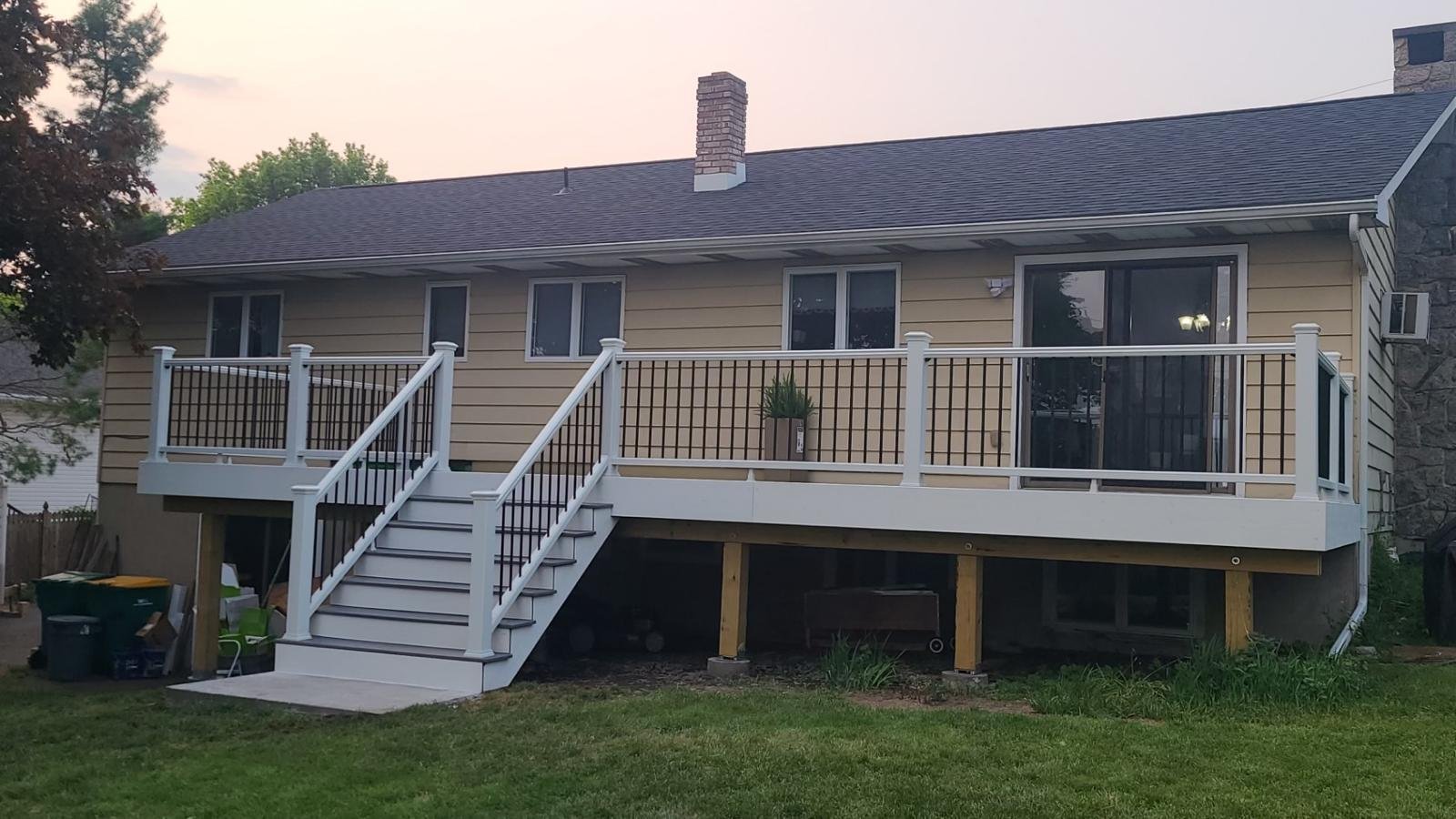 Backyard view of a house with a new deck, white railing, and stairs leading down to a grassy yard.