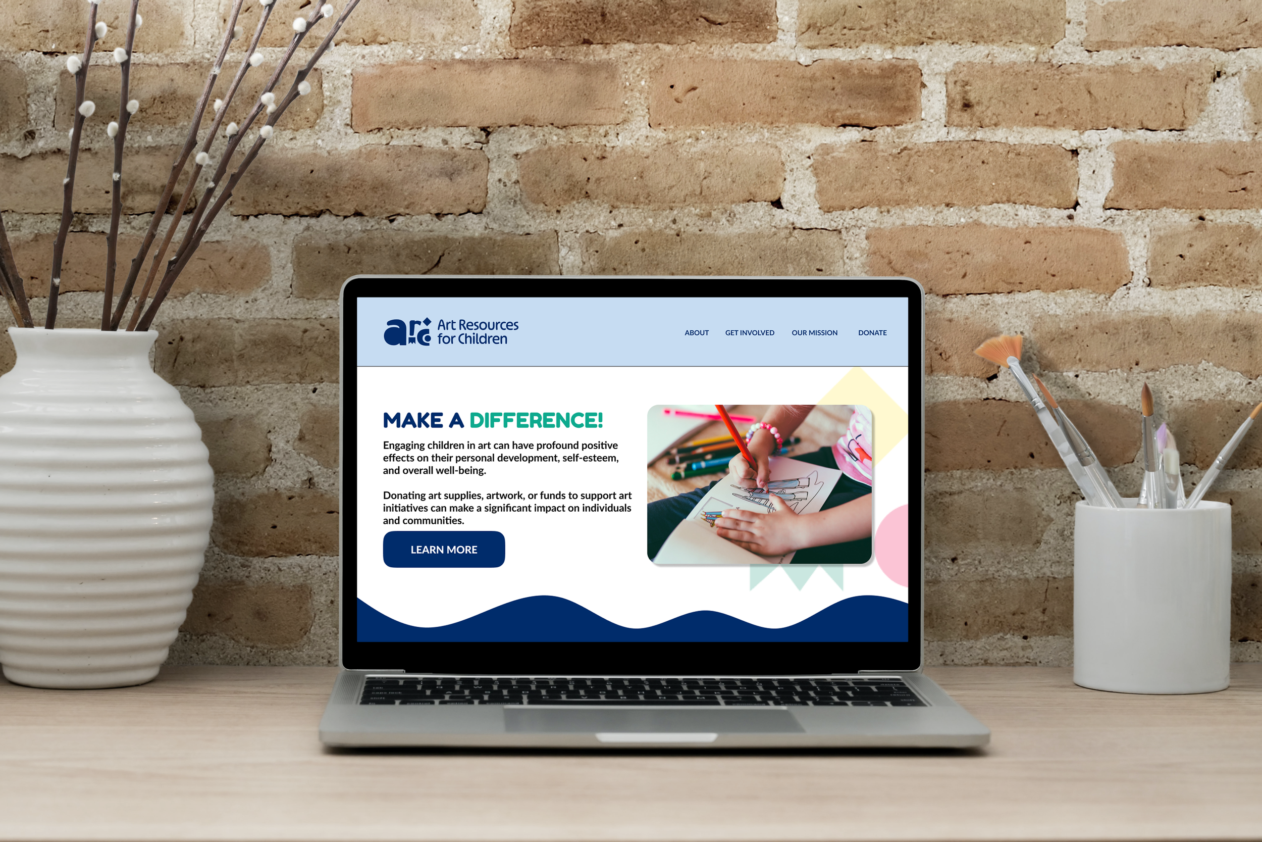 Laptop on a wooden desk displaying the website for Art Resources for Children, with the header titles "About," "Get Involved," "Our Mission," and "Donate." The webpage features a colorful section with a photo of a child coloring with crayons and a bu