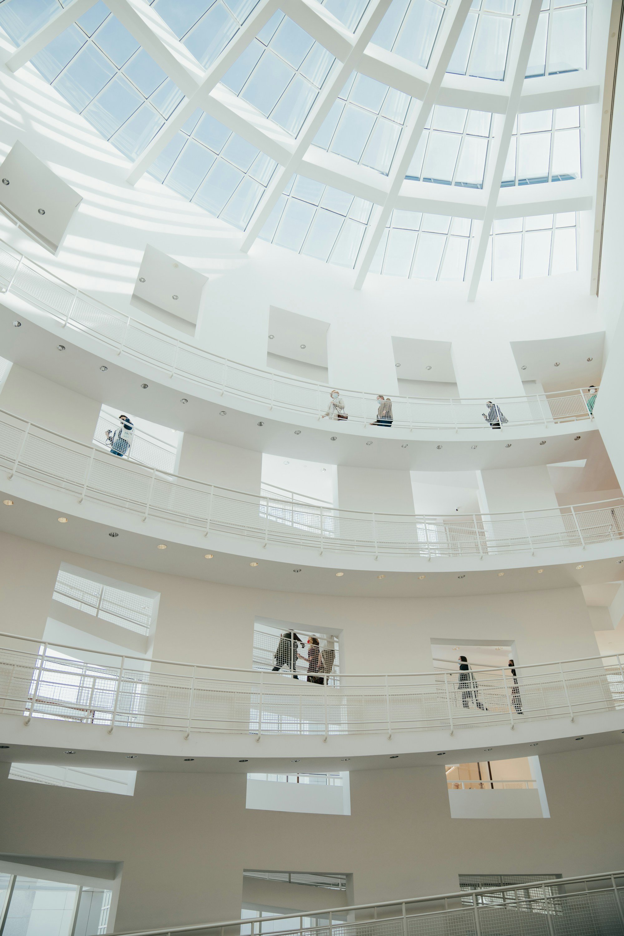 Interior view of a modern, multi-level building with white walls and railings, and a large glass dome ceiling.