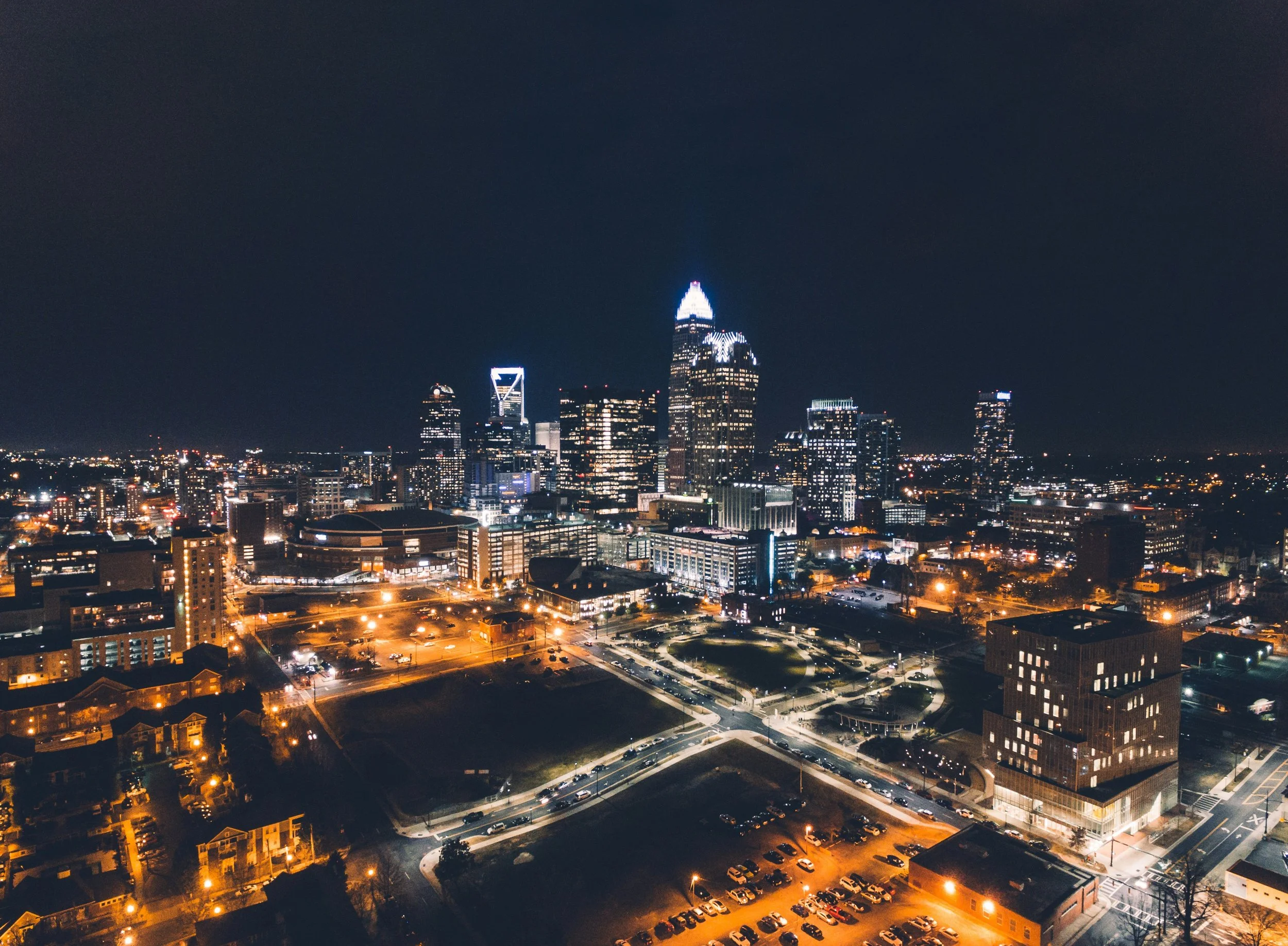 Nighttime city skyline with illuminated skyscrapers and streets, featuring a prominent, spire-topped building.