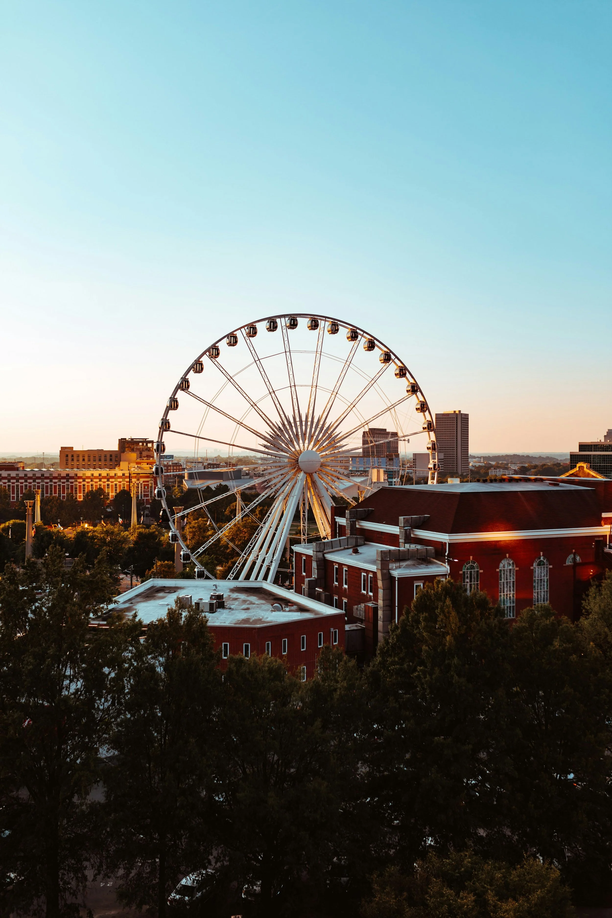 Ferris wheel behind red brick buildings during sunset in a cityscape