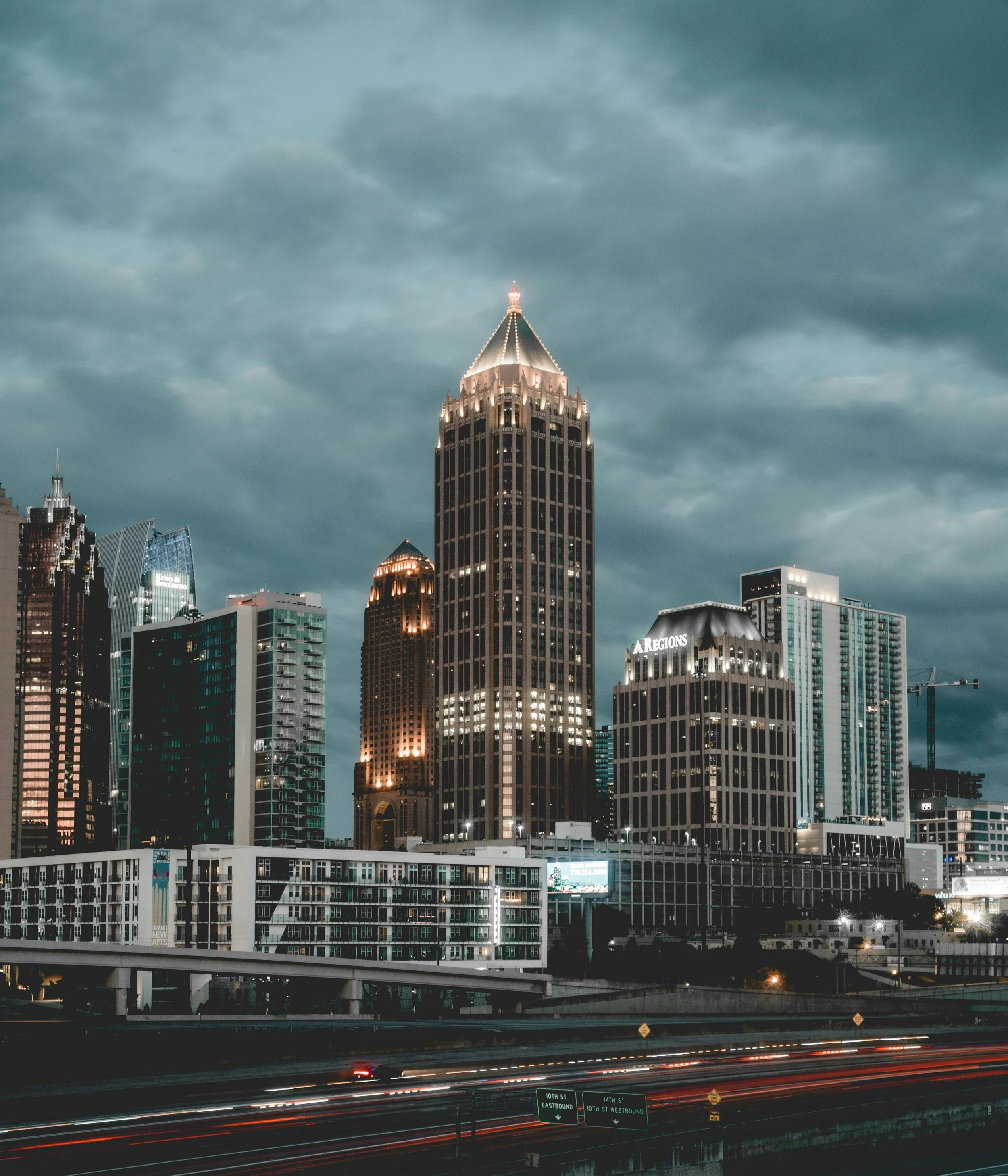 Nighttime city skyline with illuminated skyscrapers and dark cloudy sky.