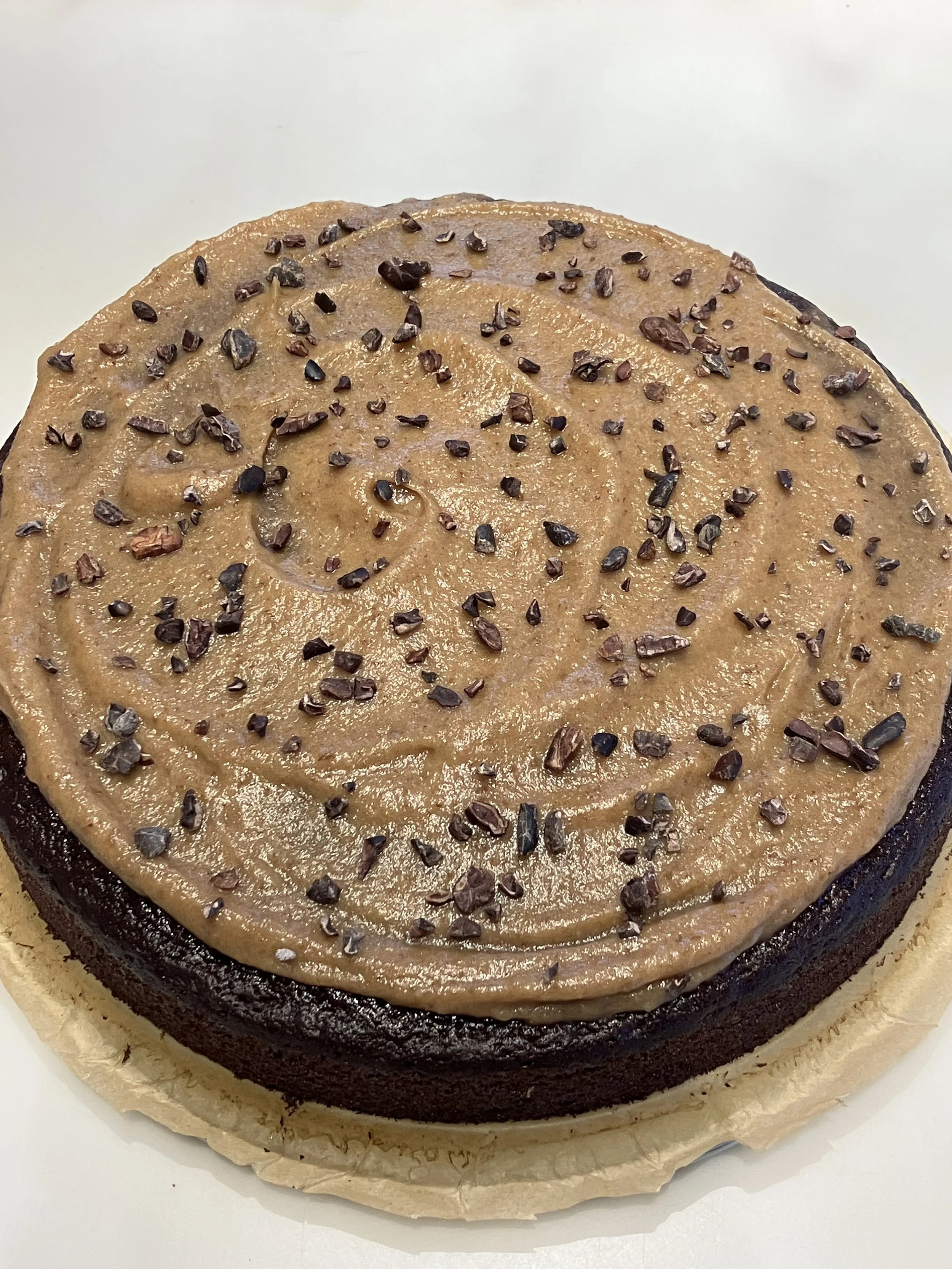 A round chocolate cake with light brown frosting and topped with chopped nuts.