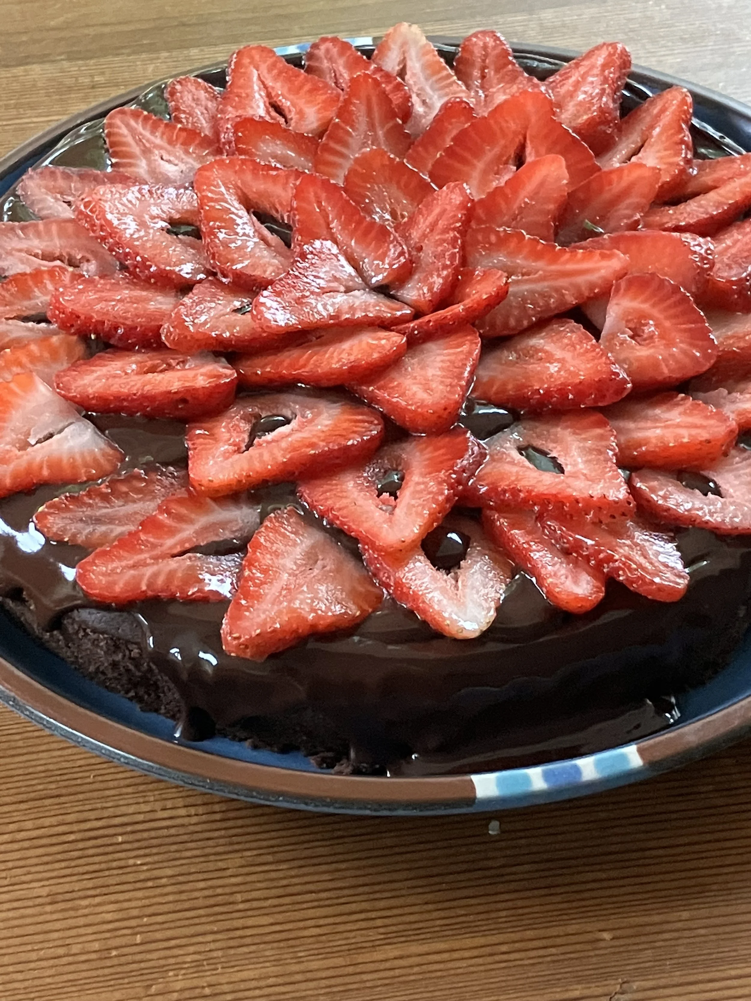 Chocolate cake topped with sliced strawberries on a metal tray.