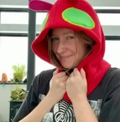 Person wearing a red hood with green accents, smiling and holding the strings of the hood.