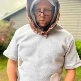 Child wearing a protective netted helmet, glasses, and a gray T-shirt outdoors.