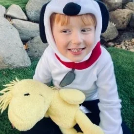 Child dressed in a dog costume smiling while holding a yellow plush toy