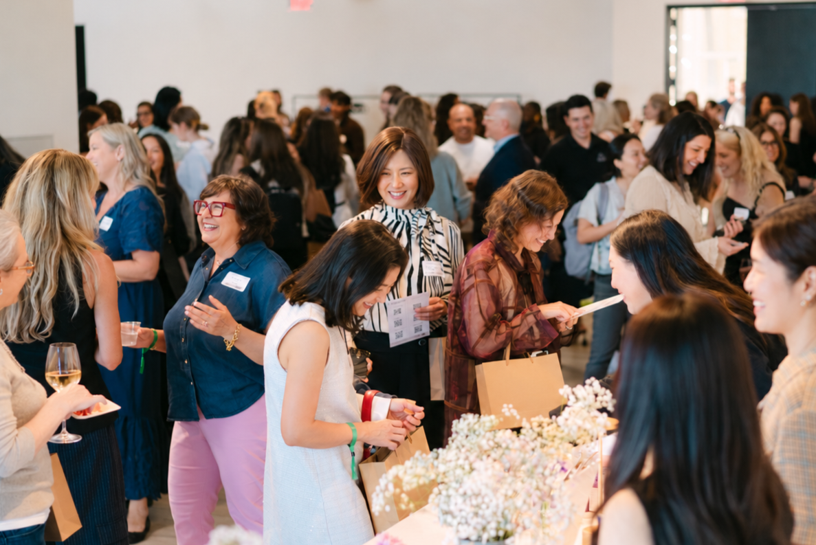 A large group of people gathered indoors at a social event or conference, engaging in conversations and smiling.
