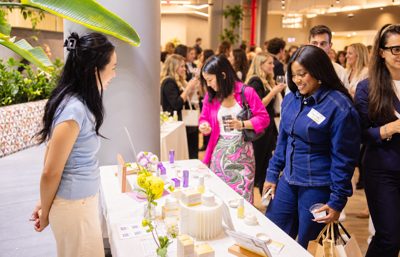 Women at a skincare or beauty product booth during a trade show or event, engaging with products on display.