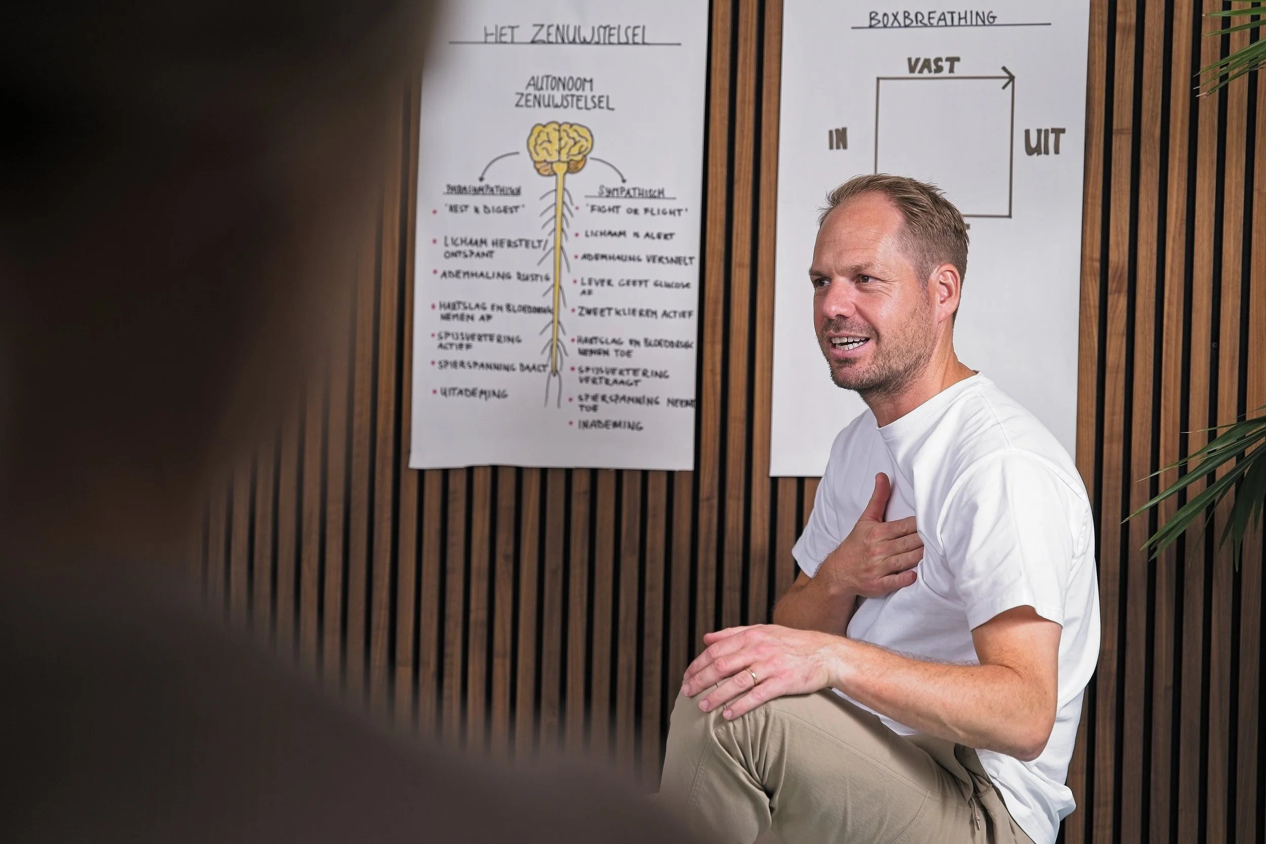 Man geeft een uitleg over het zenuwstelsel bij een lezing, met posters op de achtergrond.