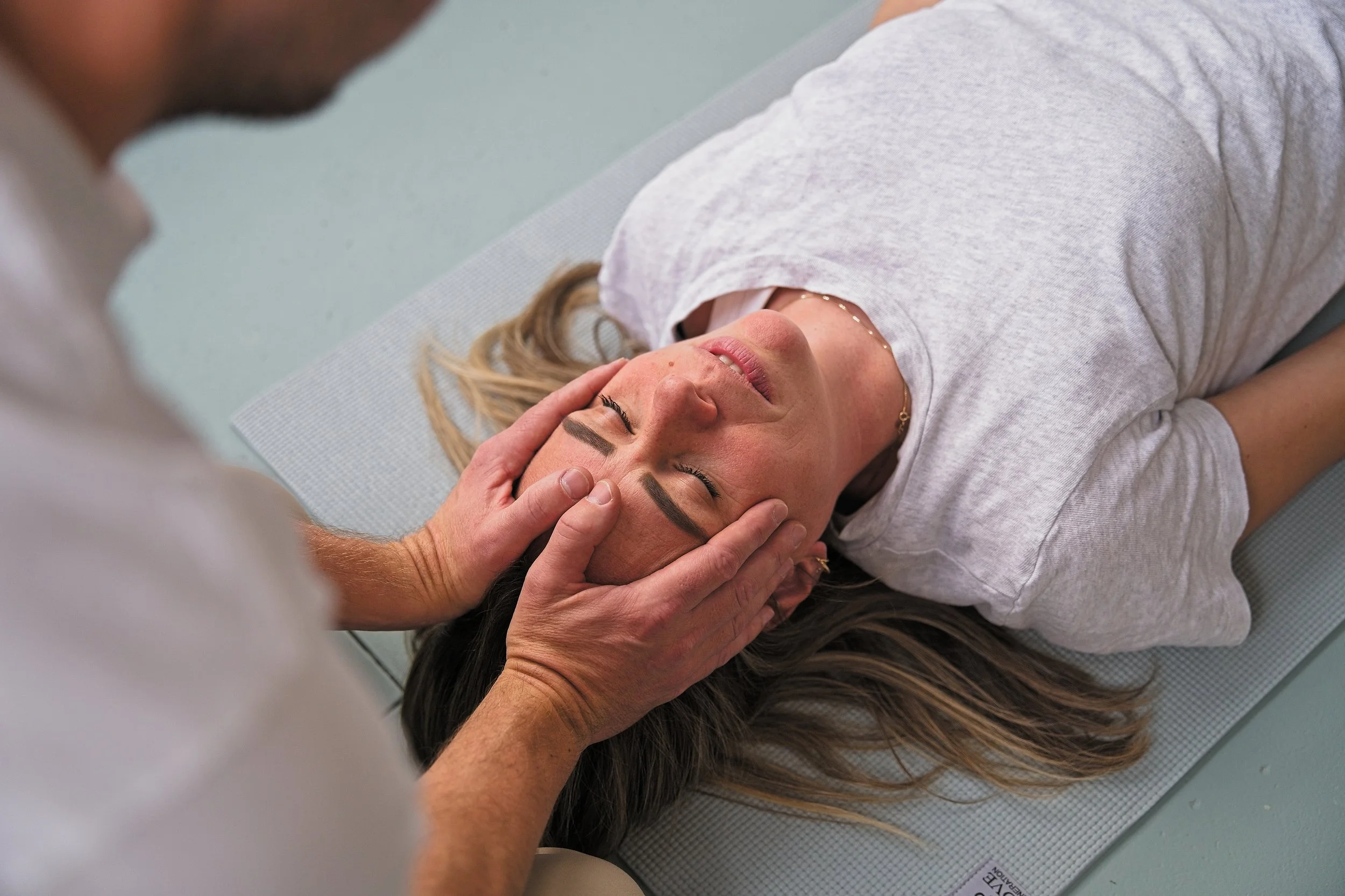 Vrouw ligt op yoga mat en krijgt een hoofdmassage van een man.