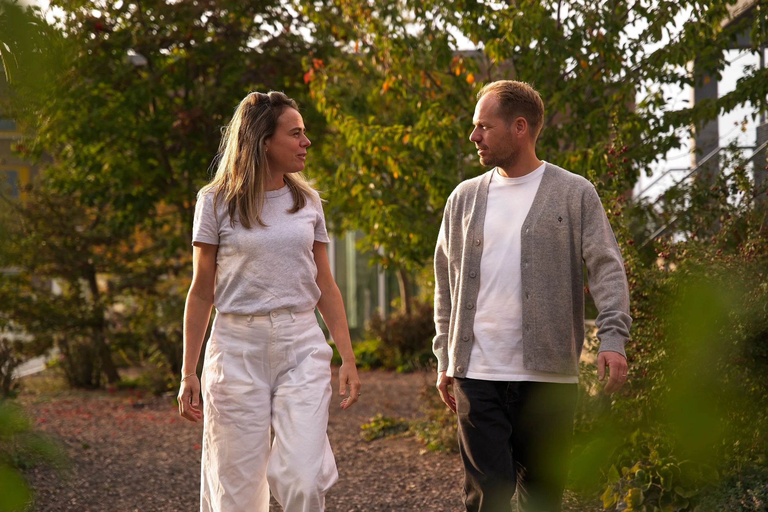 Een man en een vrouw wandelen samen in een park met herfstbladeren en bomen op de achtergrond.