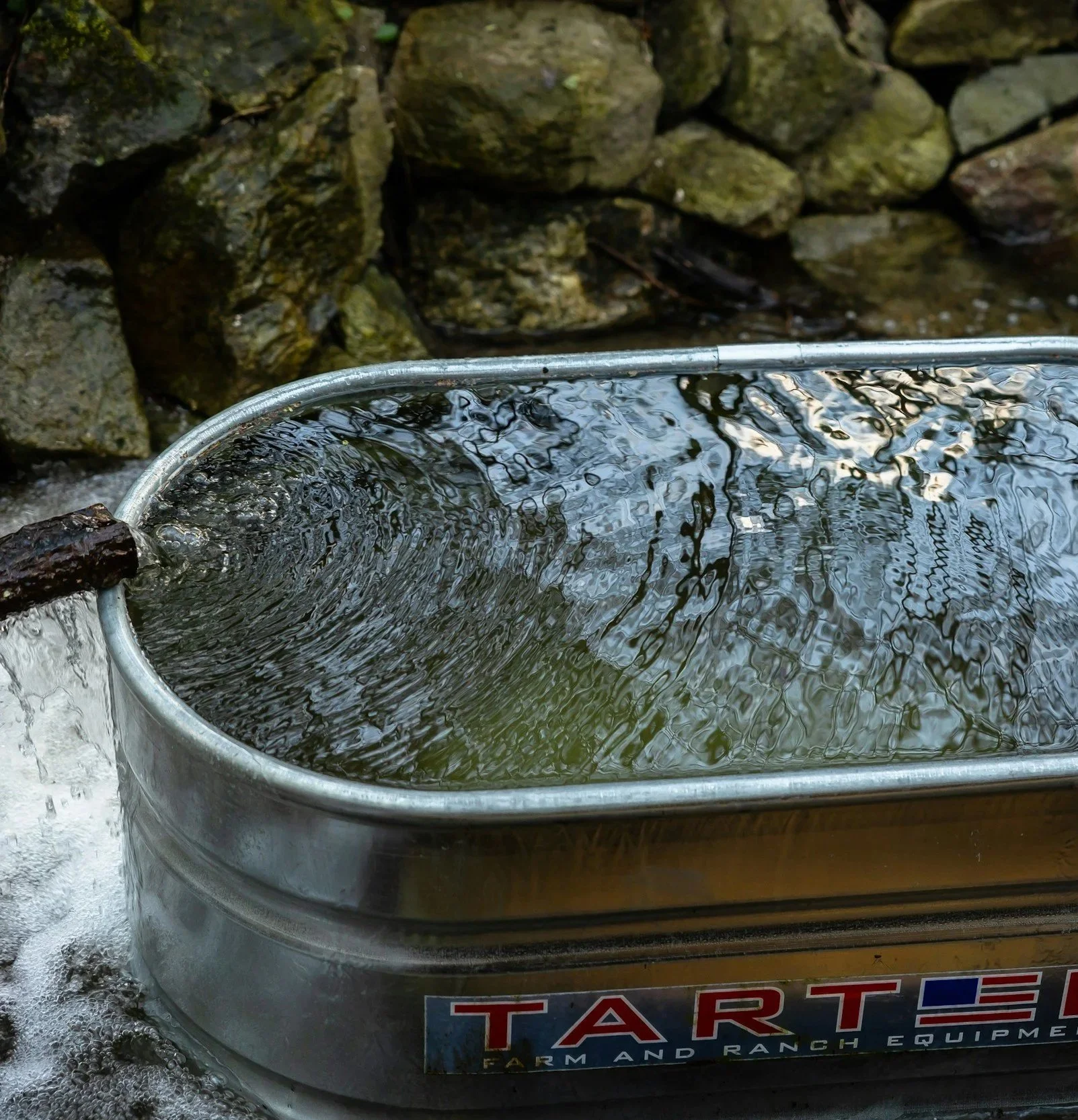 Een metalen emmer gevuld met water die borrelt, met een stenen muur op de achtergrond.