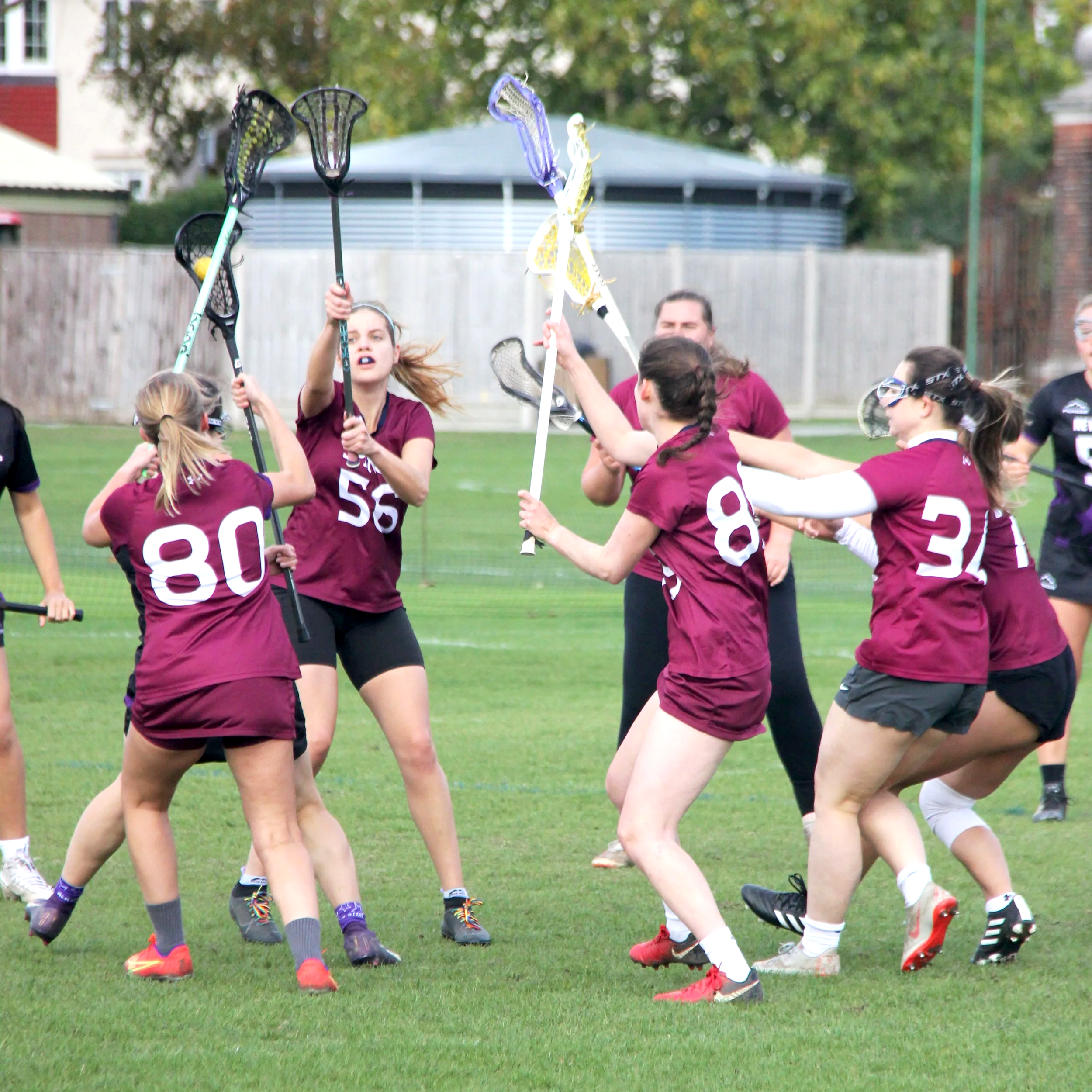 Girls' lacrosse players in maroon jerseys are fighting for possession of the ball on the field.