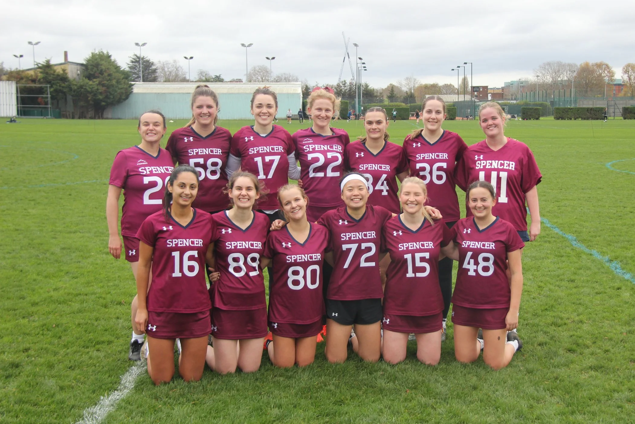 A women's lacrosse team wearing maroon jerseys and shorts on a grassy field.