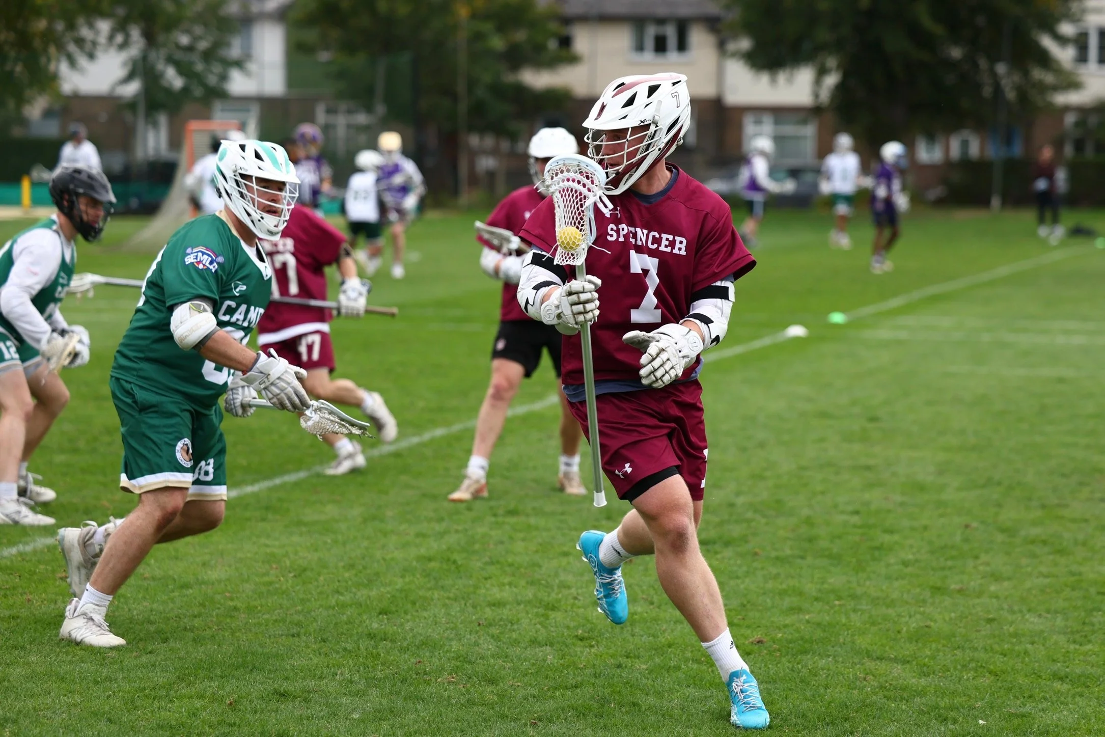 Lacrosse players in helmets and uniforms playing on a grassy field