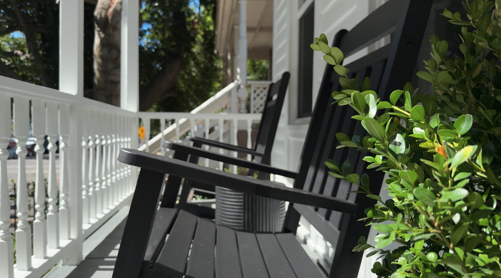 Three black wooden porch chairs on a white porch, with green bushes and trees in the background.
