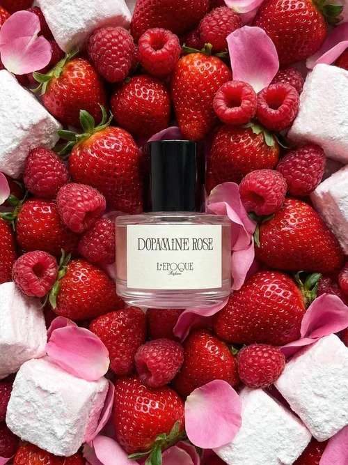 A bottle of L'EPOQUE Dopamine Rose perfume surrounded by raspberries, pink rose petals, marshmallows, and pink fabric.