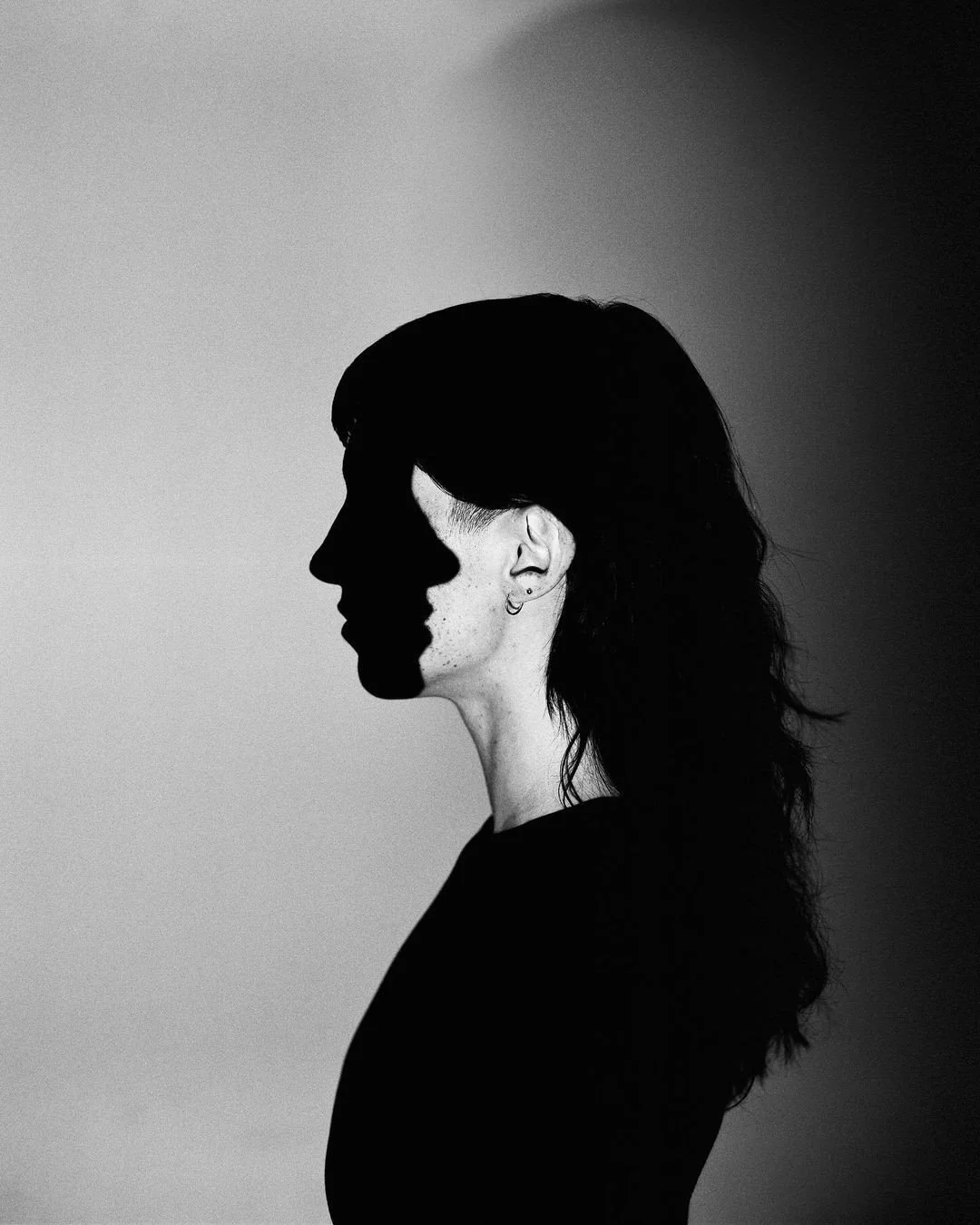 A black and white side profile of a woman with medium-length hair, with her face cast in shadow on a plain background.