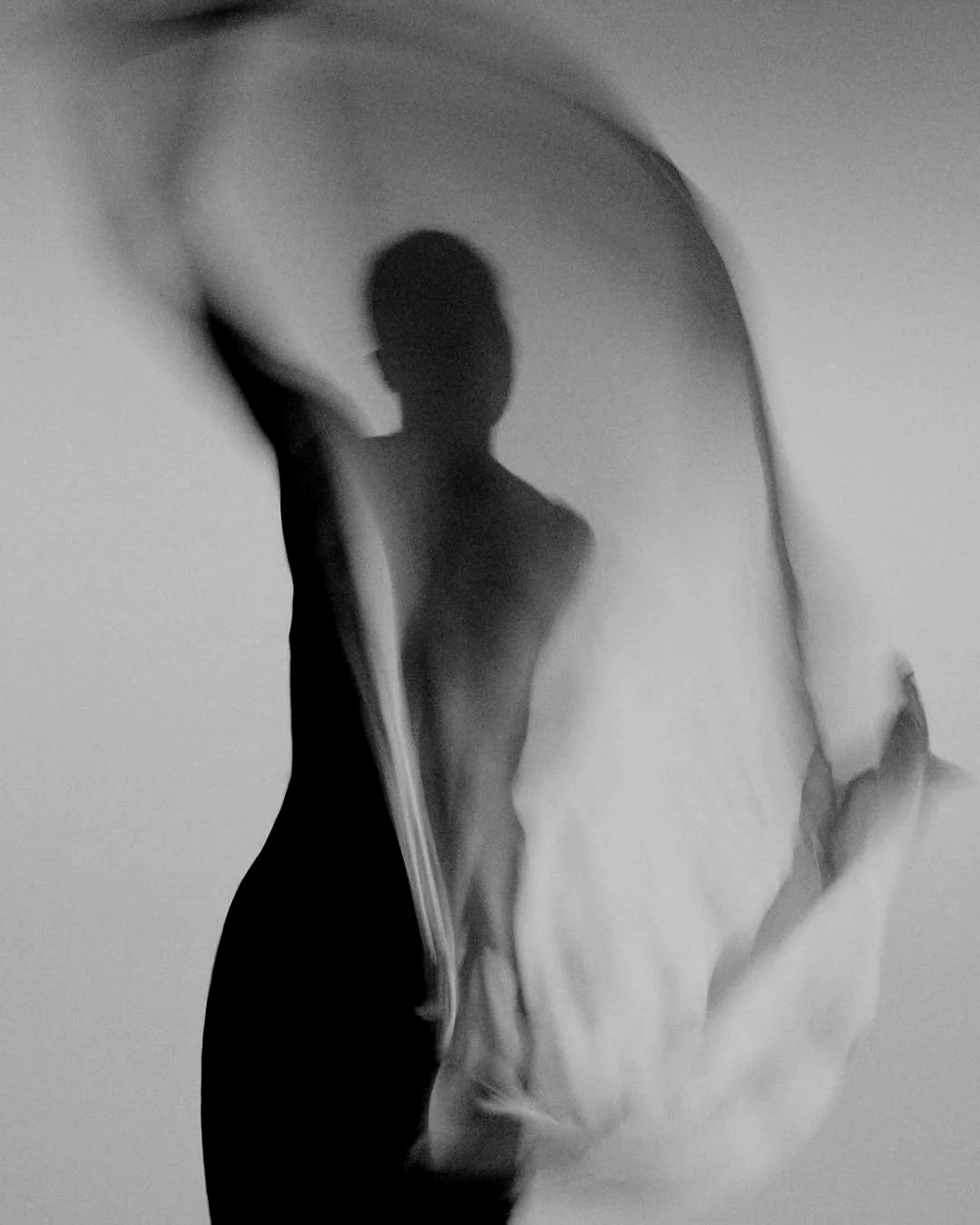 A silhouette of a person seen through a curved, transparent surface, likely a mirror or glass.