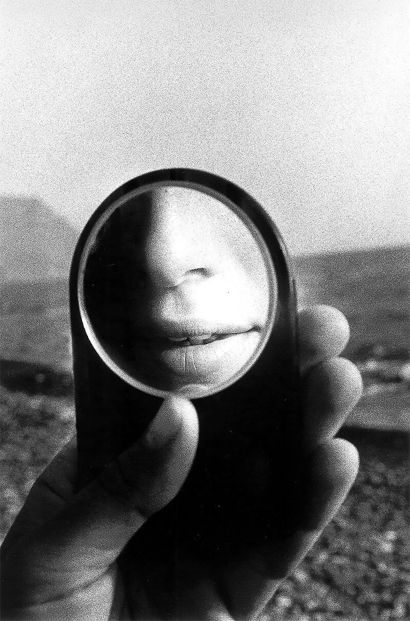 A hand holding a small mirror in front of lips and nose, reflecting a close-up of the person's face.