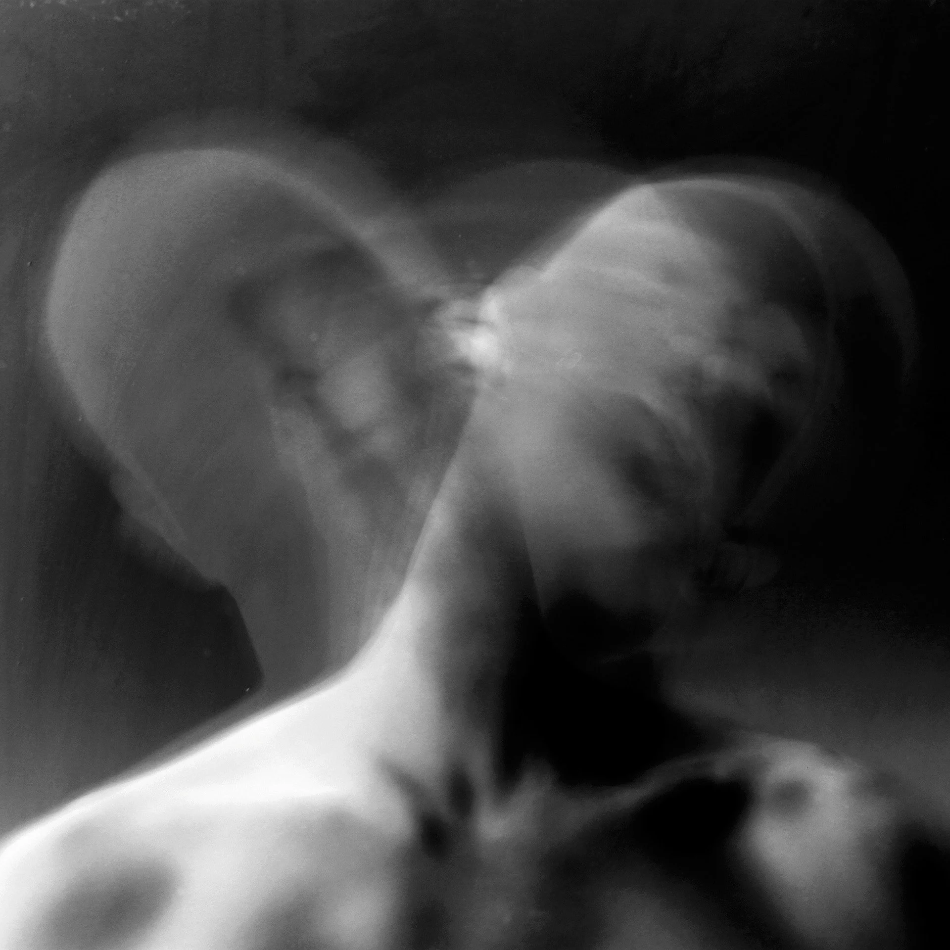 Black and white abstract photograph of two faces with their foreheads touching, creating a heart shape.