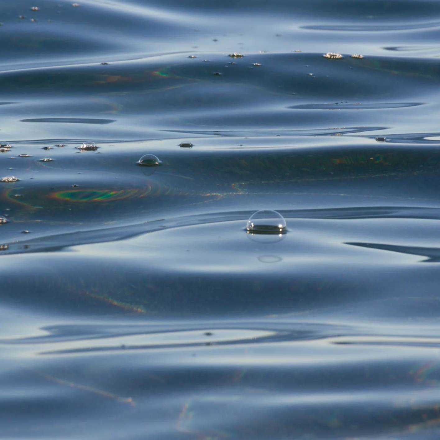 Close-up of ocean waves with small bubbles and ripples on the surface.